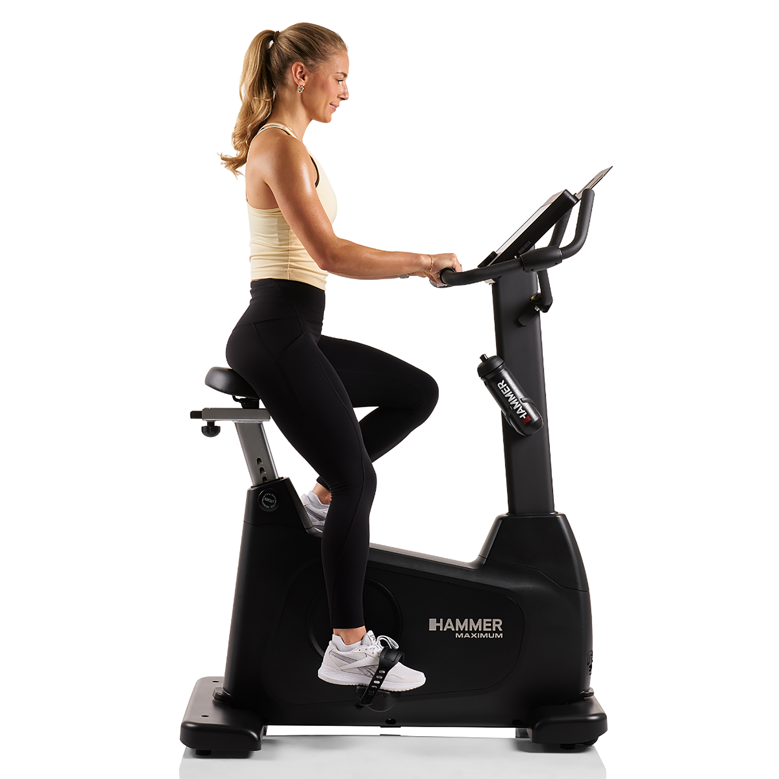 Eine Frau trainiert auf einem schwarzen Heimtrainer, trägt schwarze Leggings und ein gelbes Oberteil.