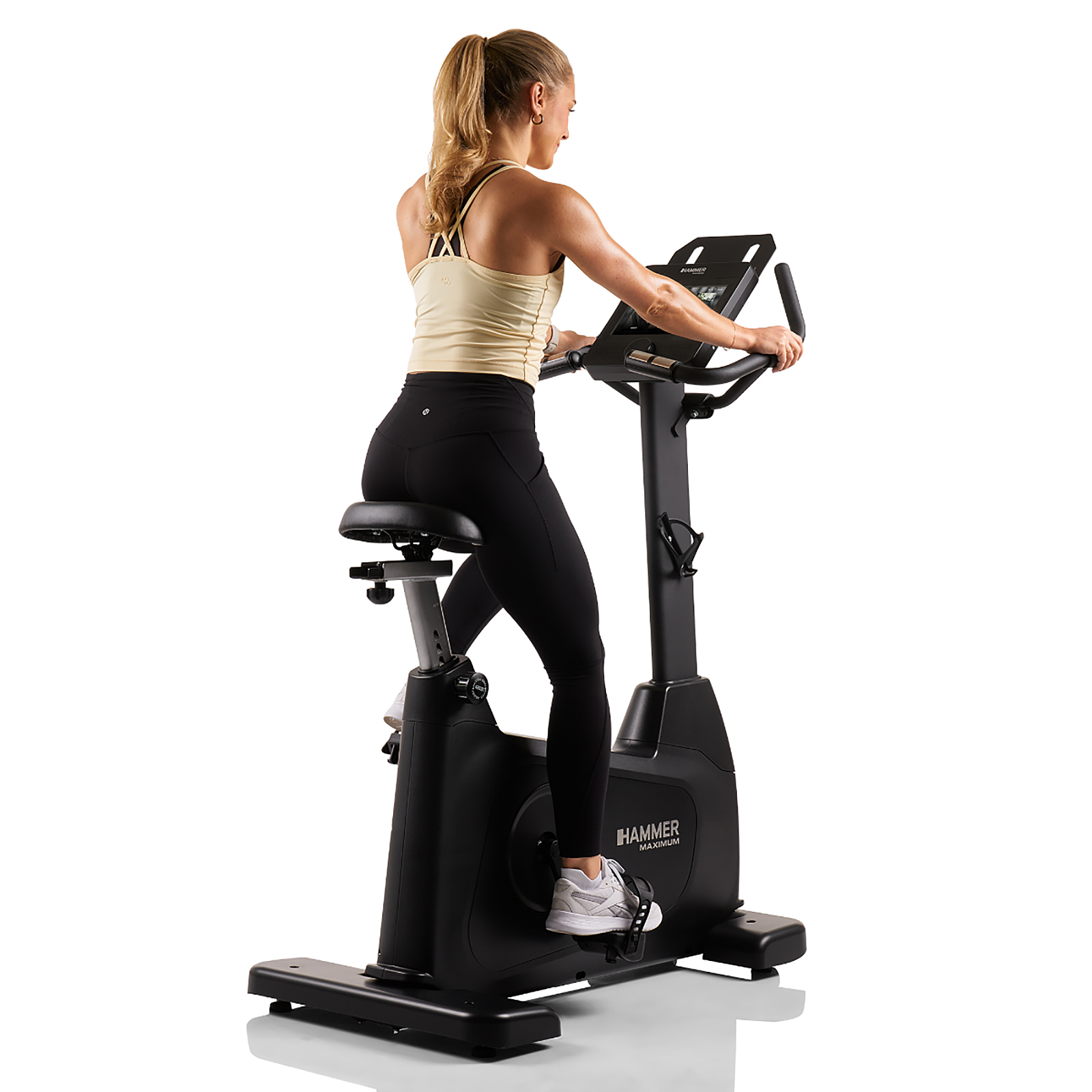 Eine Frau auf einem schwarzen Heimtrainer, mit sichtbarem Display, fährt auf den Betrachter zu.