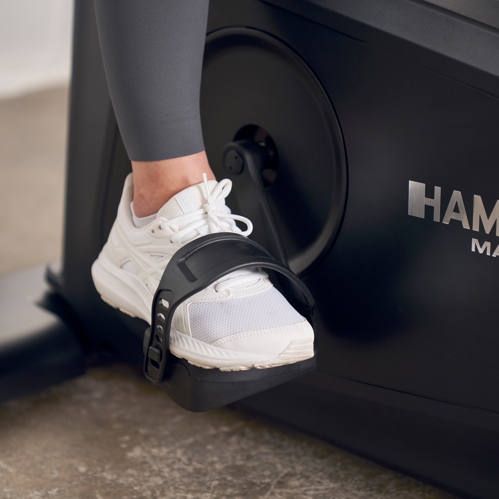 Nahaufnahme des Fußes einer Person mit einem weißen Turnschuh auf einer Heimtrainer-Pedale.