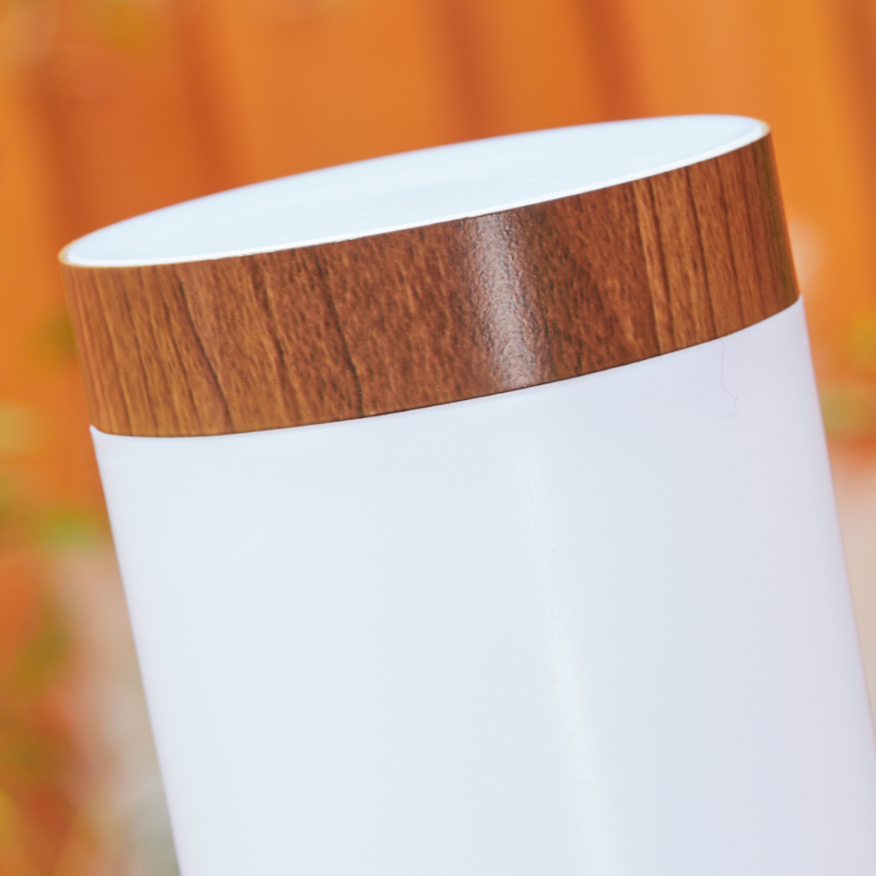 Weißer Zylinder mit Holzdeckel. Der Hintergrund ist ein unscharfes Orange und Gelb.
