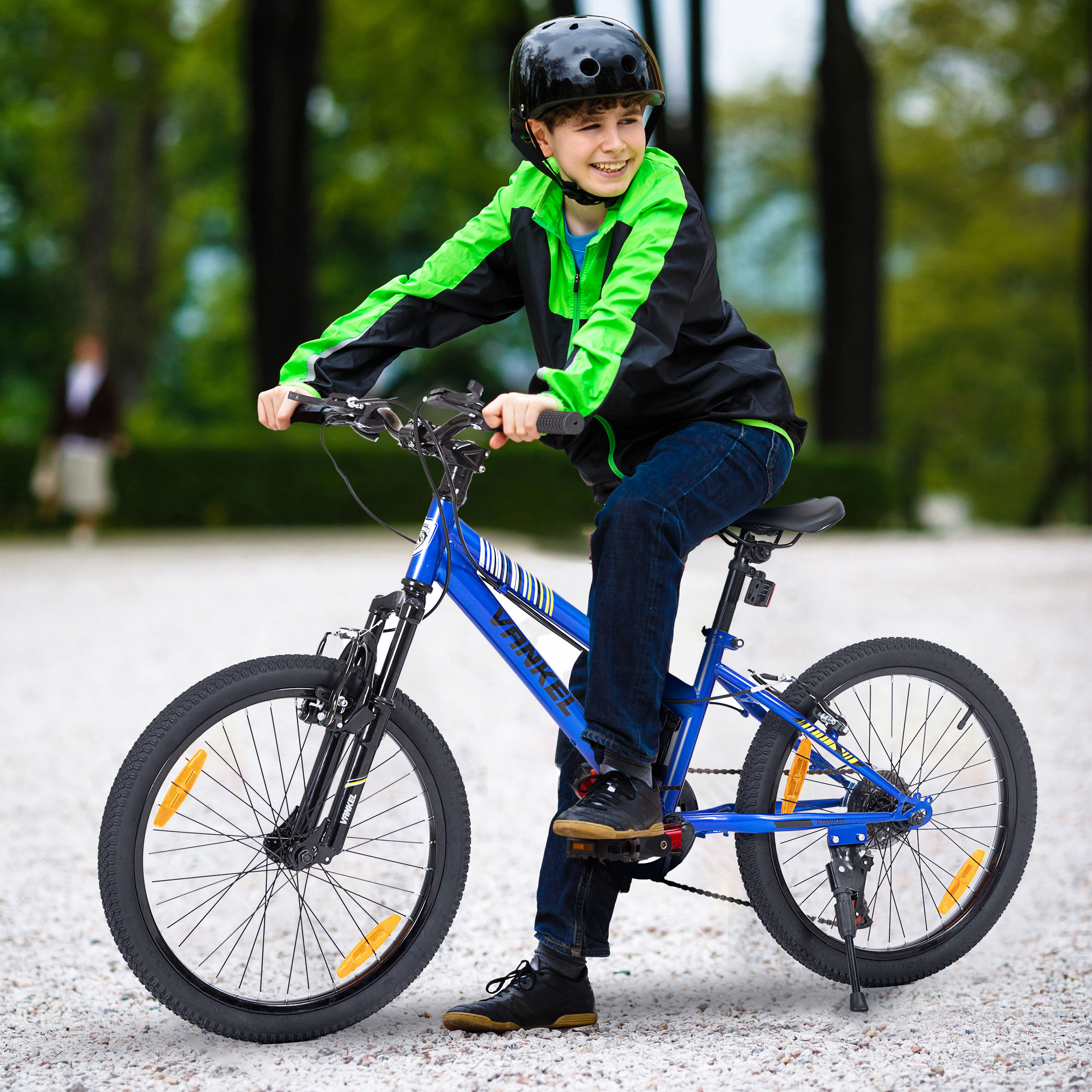 Ein Junge mit Helm fährt auf einem blauen Fahrrad auf einem Weg mit grünen Bäumen im Hintergrund.