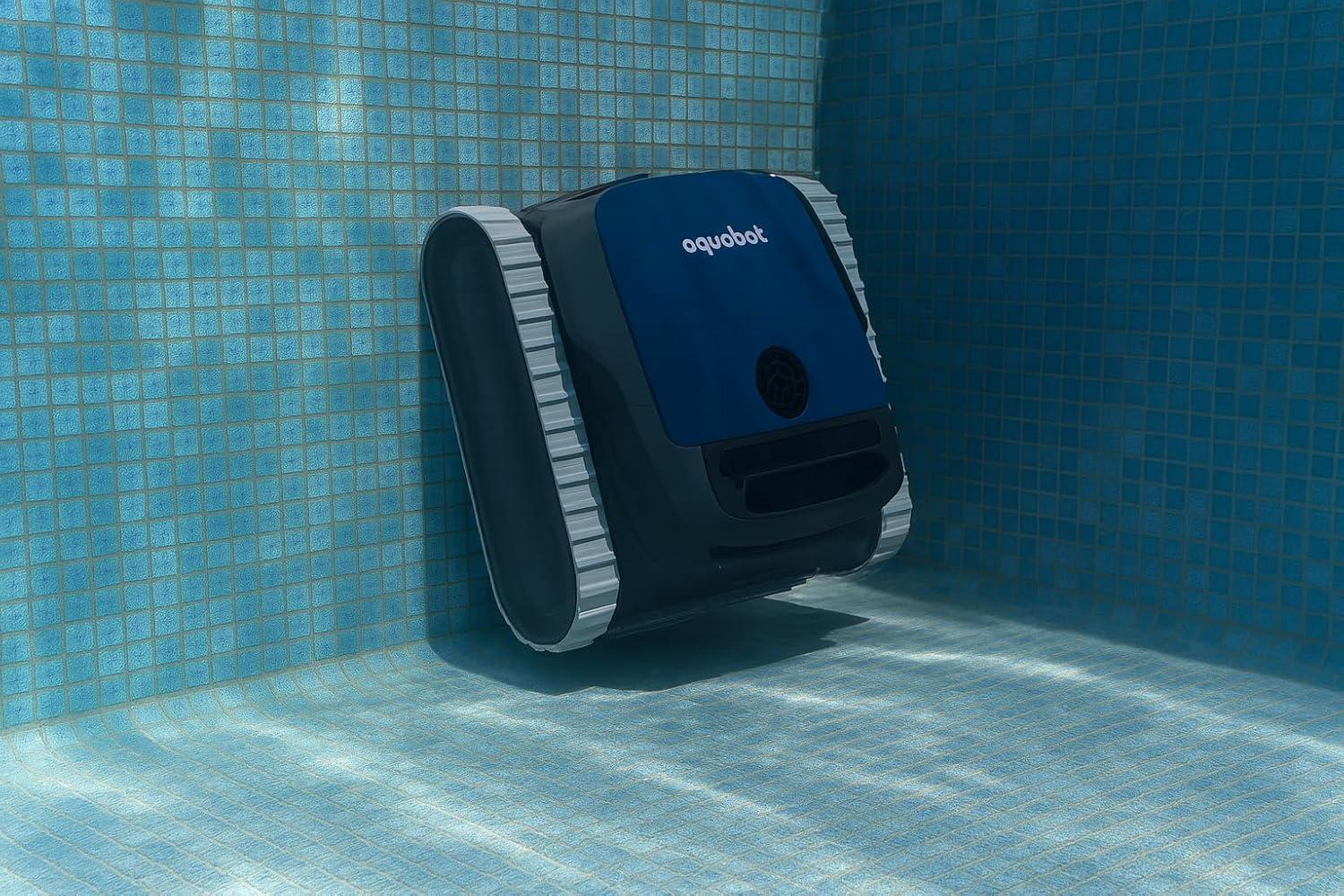 Un limpiador de piscinas robótico azul y gris sumergido en una piscina con paredes de azulejos azules y agua clara.