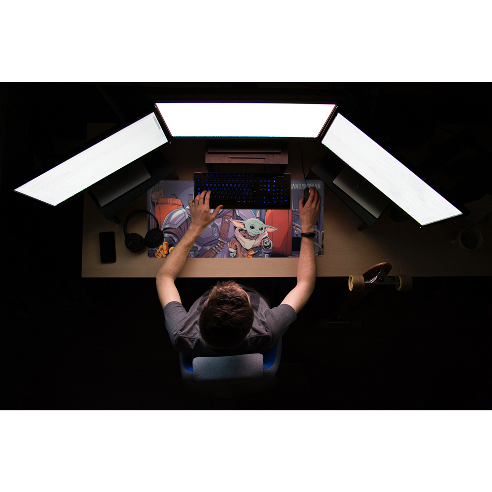 Draufsicht einer Person, die ein Mauspad mit The Mandalorian und Grogu benutzt. Drei Monitore, eine Tastatur und ein Skateboard sind vorhanden.