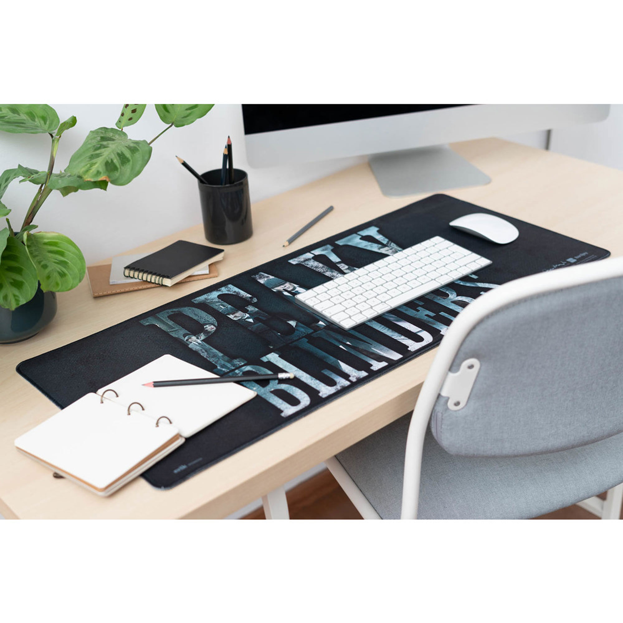 Schreibtisch-Setup mit Computer, Tastatur, Maus und Notizblock auf einem schwarzen Mousepad.