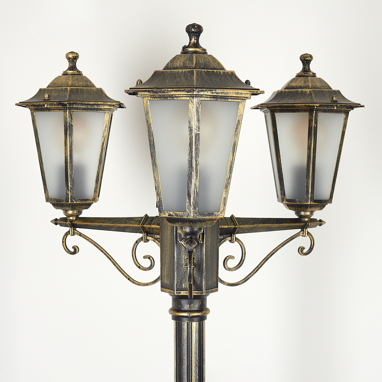 Dreifach-Lampen-Laternenpfahl in Gold und Schwarz auf weißem Hintergrund. Die Lampen haben Milchglas und Verzierungen.