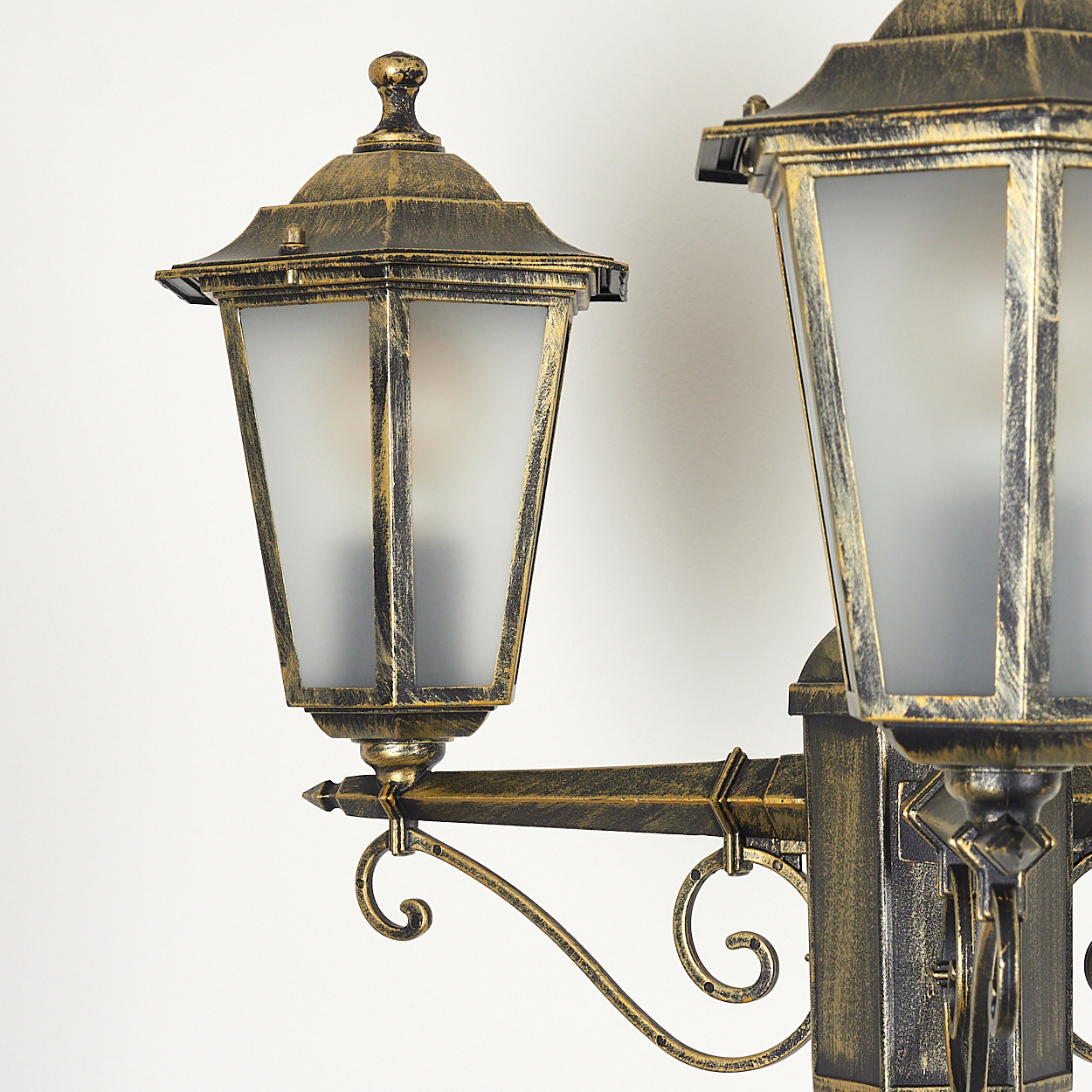 Nahaufnahme eines gold-schwarzen Laternenpfahls mit zwei Lampen. Die Lampen haben Milchglas und Verzierungen.