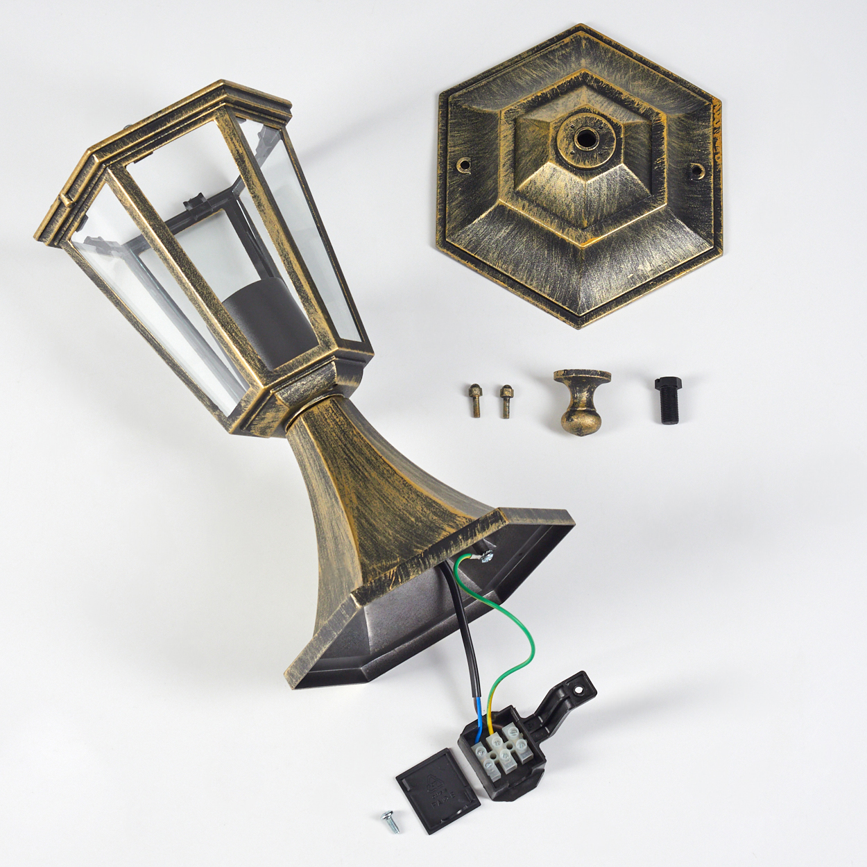 Eine bronzefarbene Lampe ist teilweise auf einer weißen Oberfläche zerlegt, mit Sockel, Leuchte und elektrischen Komponenten.