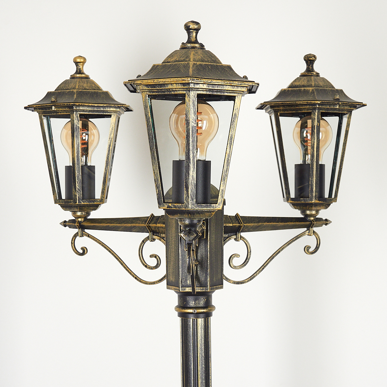 Nahaufnahme einer Straßenlaterne mit drei Lichtern. Die Lampe hat eine Gold- und Schwarz-Oberfläche.