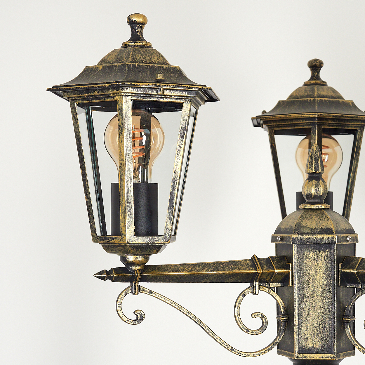 Zwei verzierte, gold-schwarze Lampen mit Glasscheiben. Ein weißer Hintergrund mit Zierdesign.
