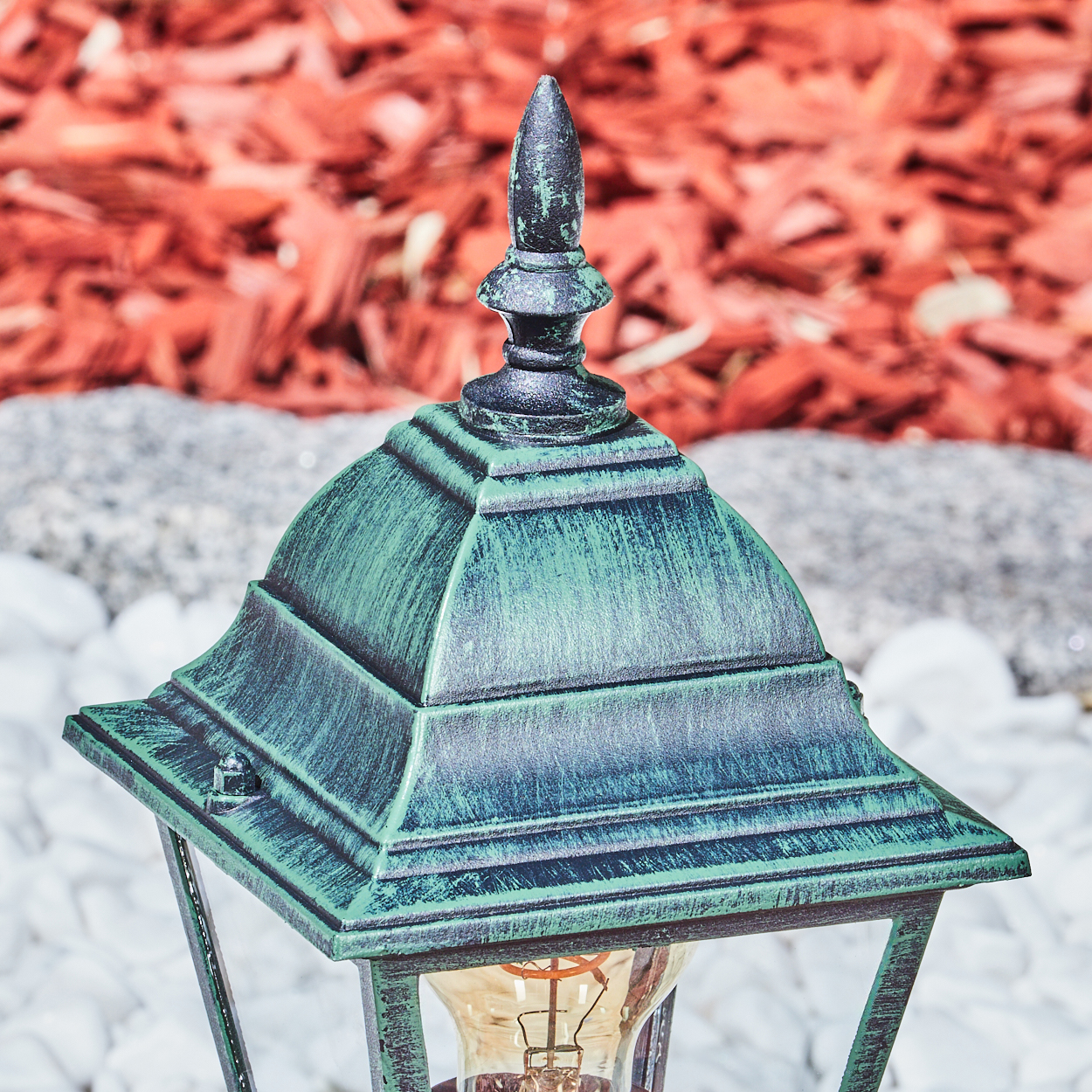 Nahaufnahme einer grün-schwarzen Außenlampe. Rote Mulch im Hintergrund und weiße Steine.