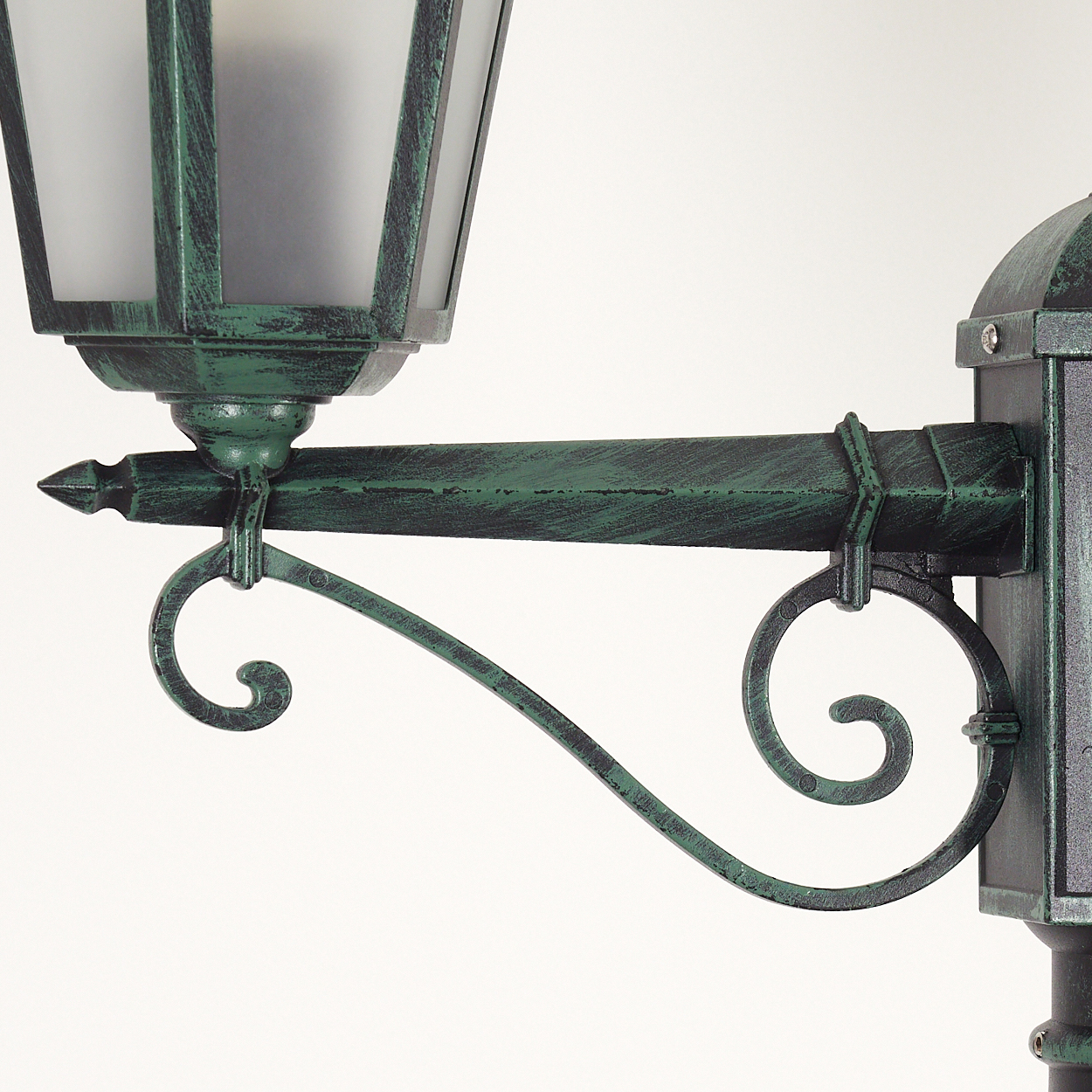 Nahaufnahme eines grünen, verzierten Straßenlampenarms mit weißem Hintergrund. Merkmale Scroll-Design.