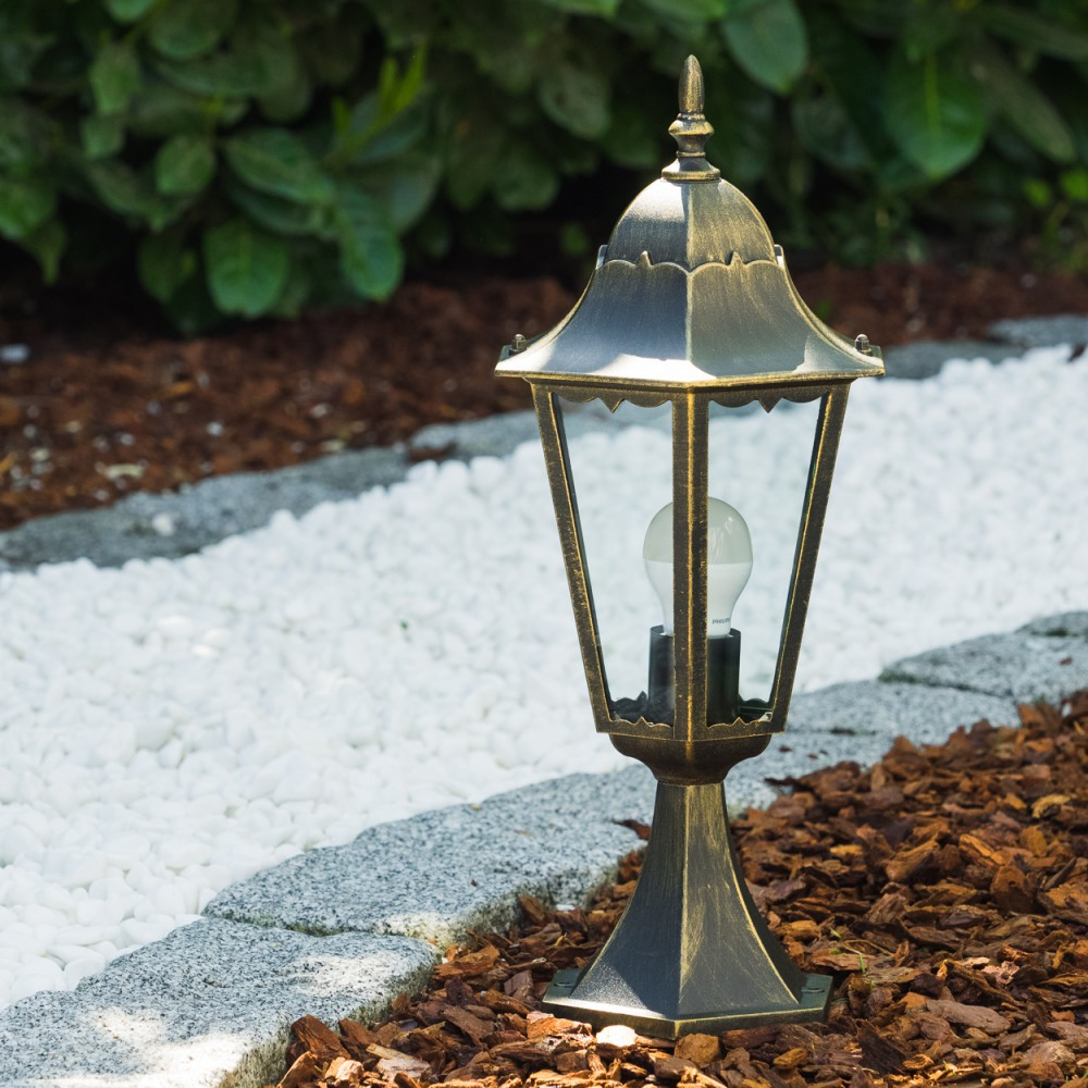 Bronze-Außenlampe in einem Garten mit weißen Steinen und Mulch.