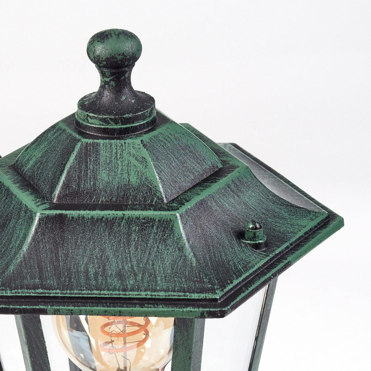 Nahaufnahme eines grünen Außenlampenaufsatzes. Die Lampe ist grün mit Glühbirne im Inneren, weißer Hintergrund.
