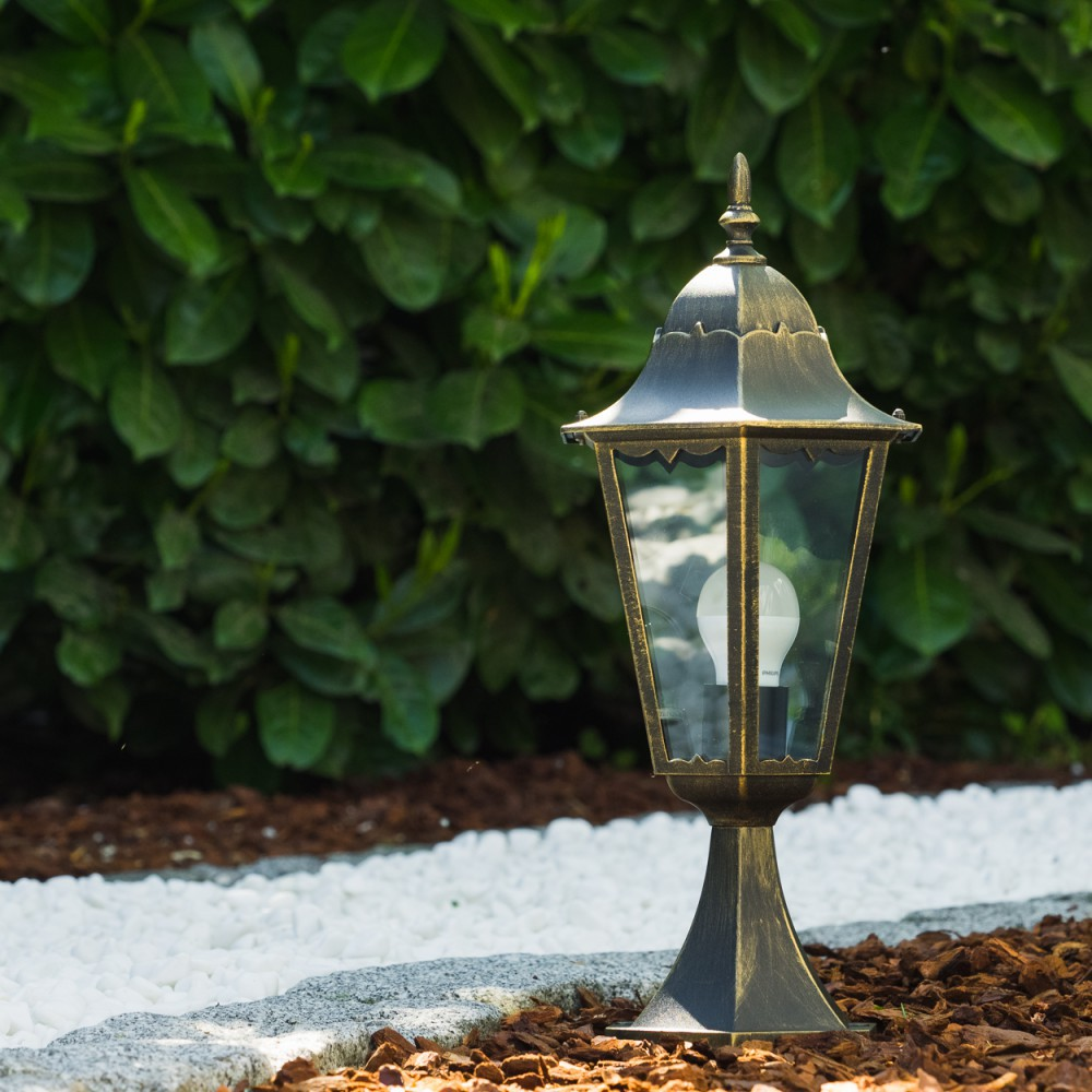 Bronze-Außenlampe in einem Garten, mit weißen Steinen und Mulch.
