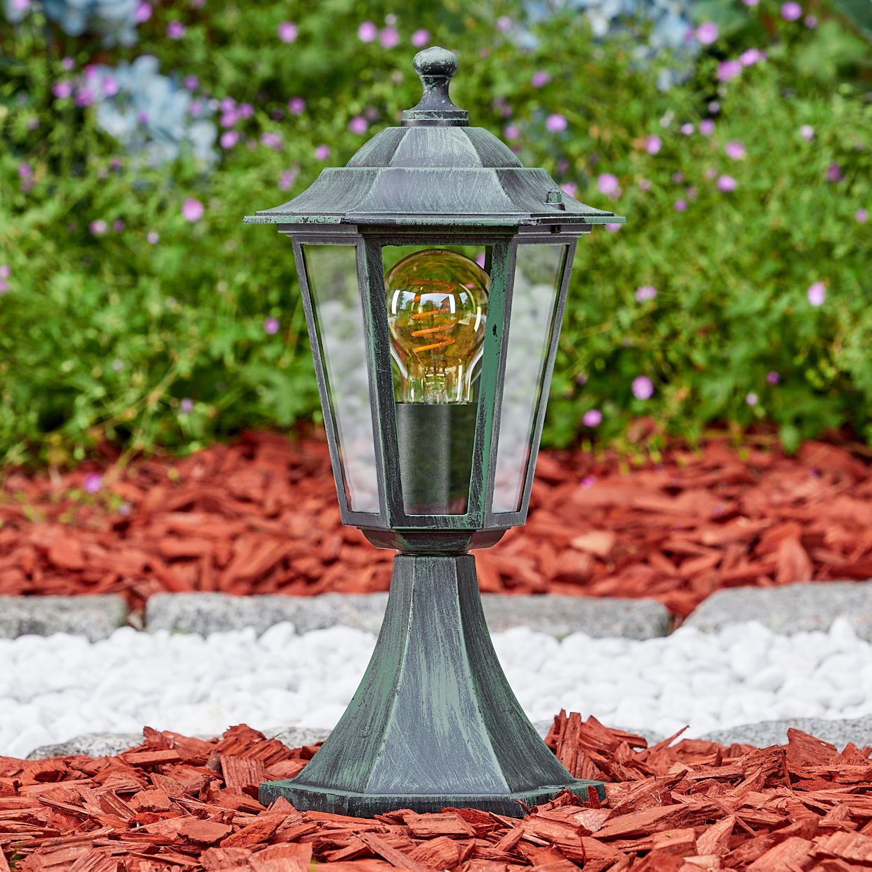 Grüne Lampe auf roter Mulch. Glühbirne im Glas. Busch im Hintergrund.