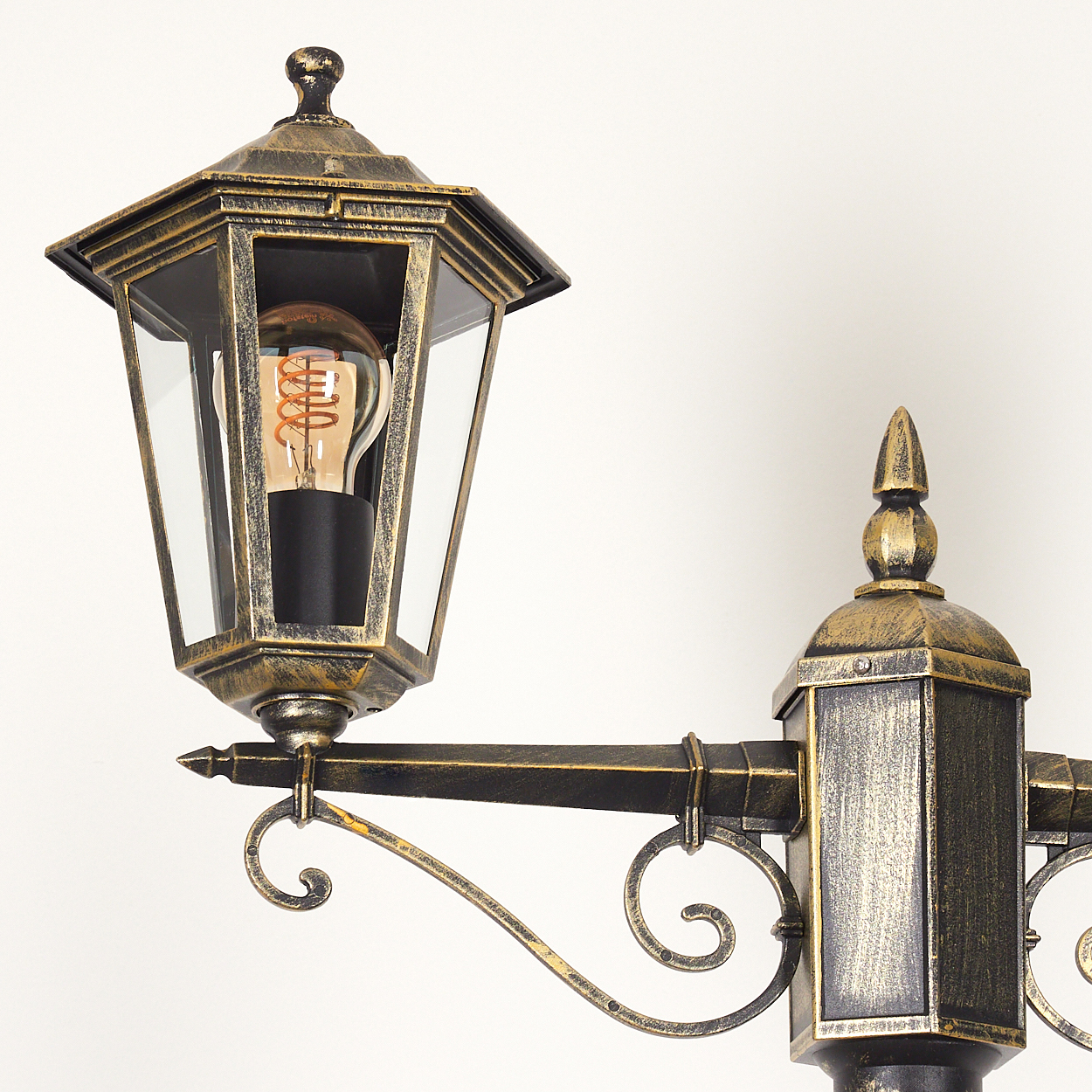 Außenlampe mit Glühbirne, Gold und Schwarz, auf weißem Hintergrund, Nahaufnahme.