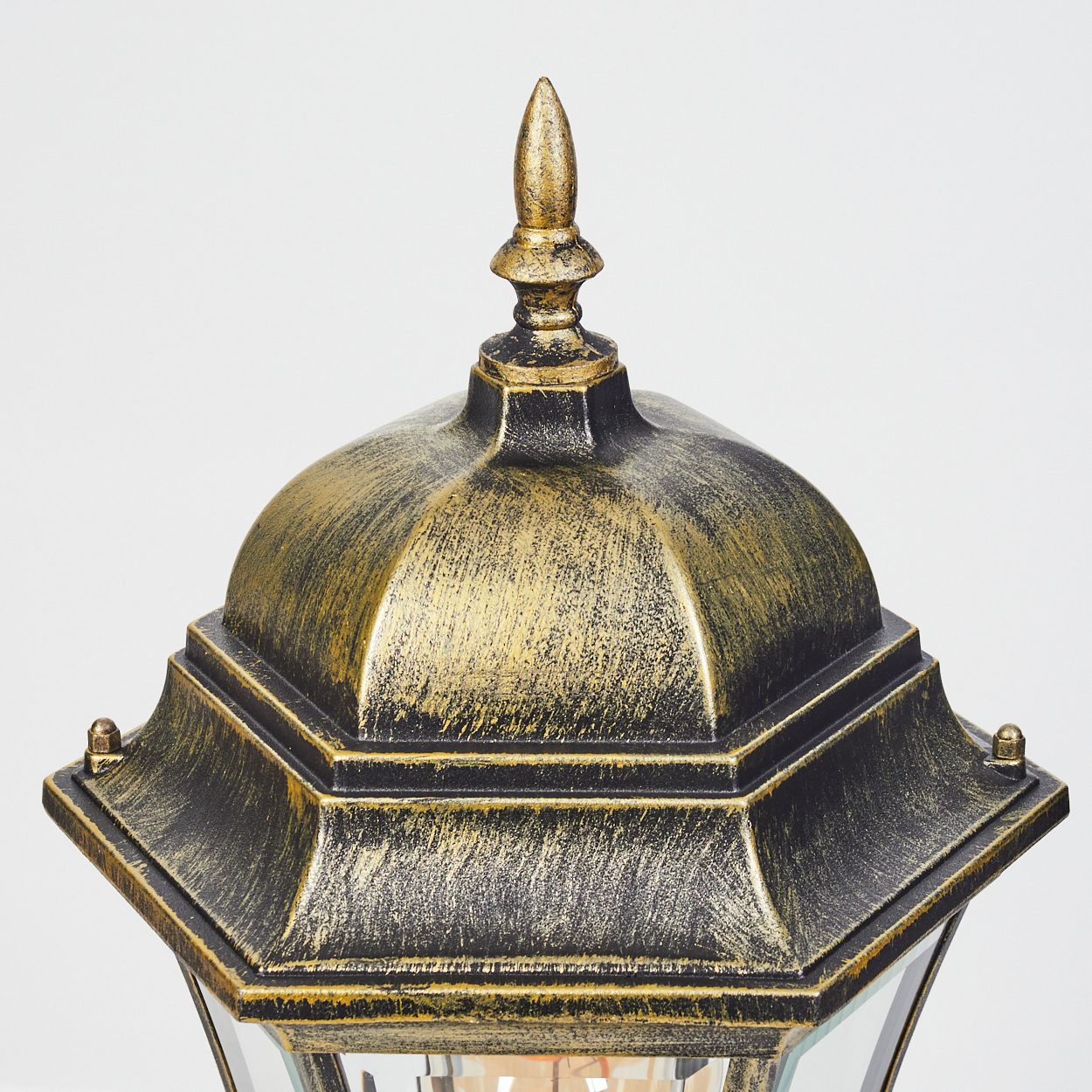 Nahaufnahme des Oberteils einer gold-schwarzen Außenlampe. Mit Zierknauf und strukturierter Oberfläche.