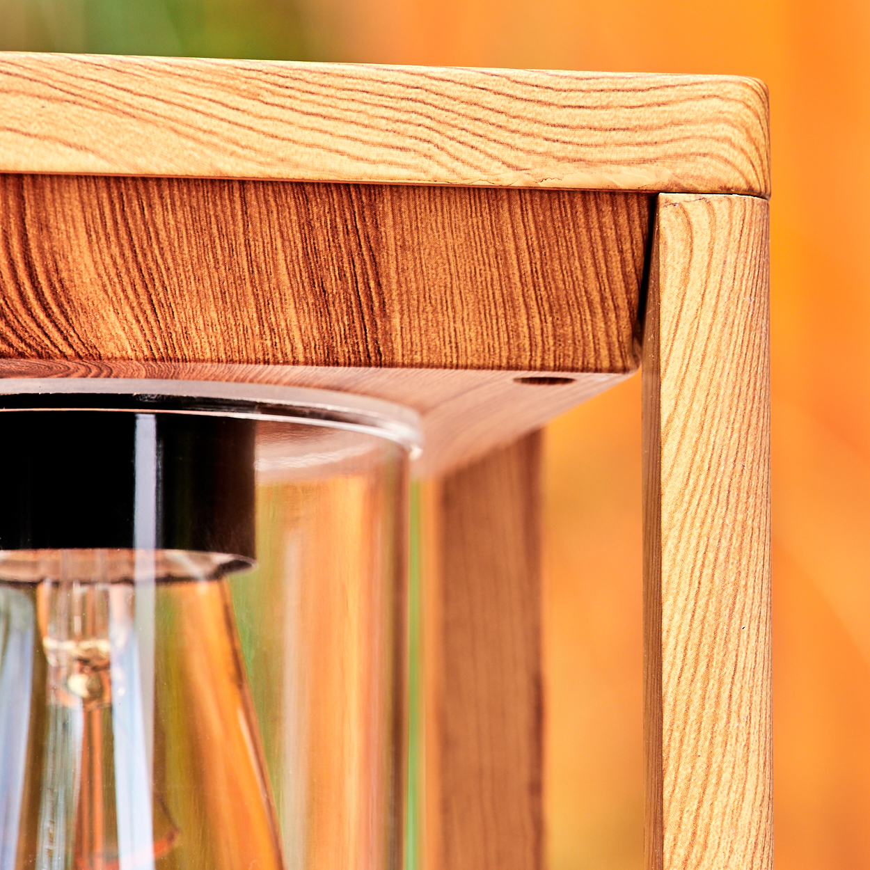 Nahaufnahme der Holzlampe mit Glühbirne in einem Glasrohr. Der Hintergrund ist mit Grün und Orange verschwommen.