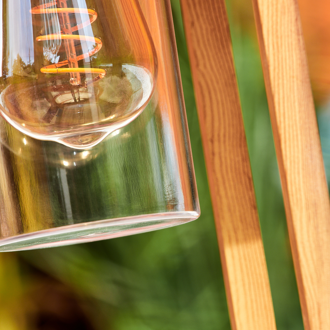 Nahaufnahme einer Holzlampe mit Glühbirne in einem Glasrohr. Verschwommener grüner und oranger Hintergrund.