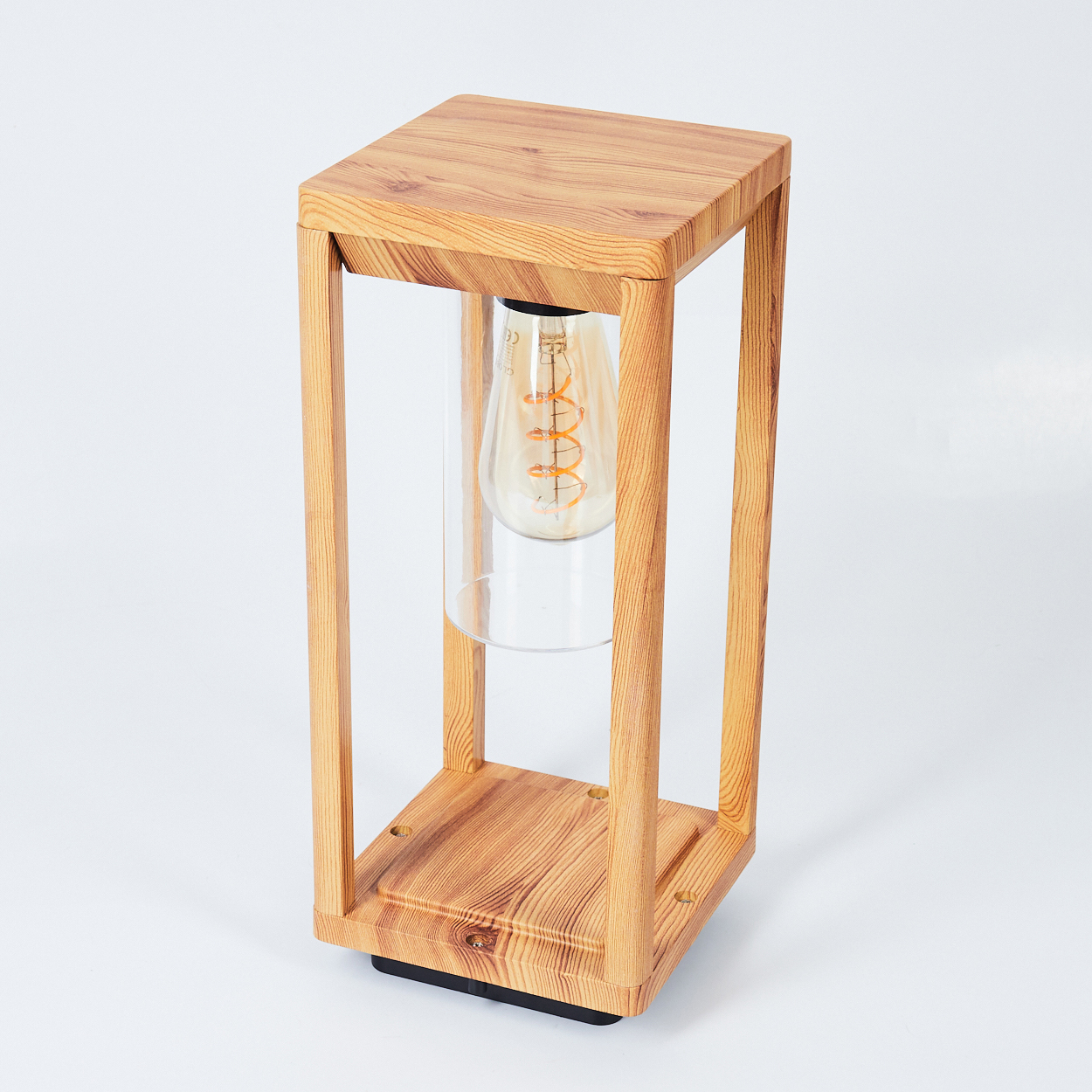 Holzlampe mit Glühbirne in einem Glasrohr. Der Sockel der Lampe ist schwarz. Sie steht auf weißem Untergrund.