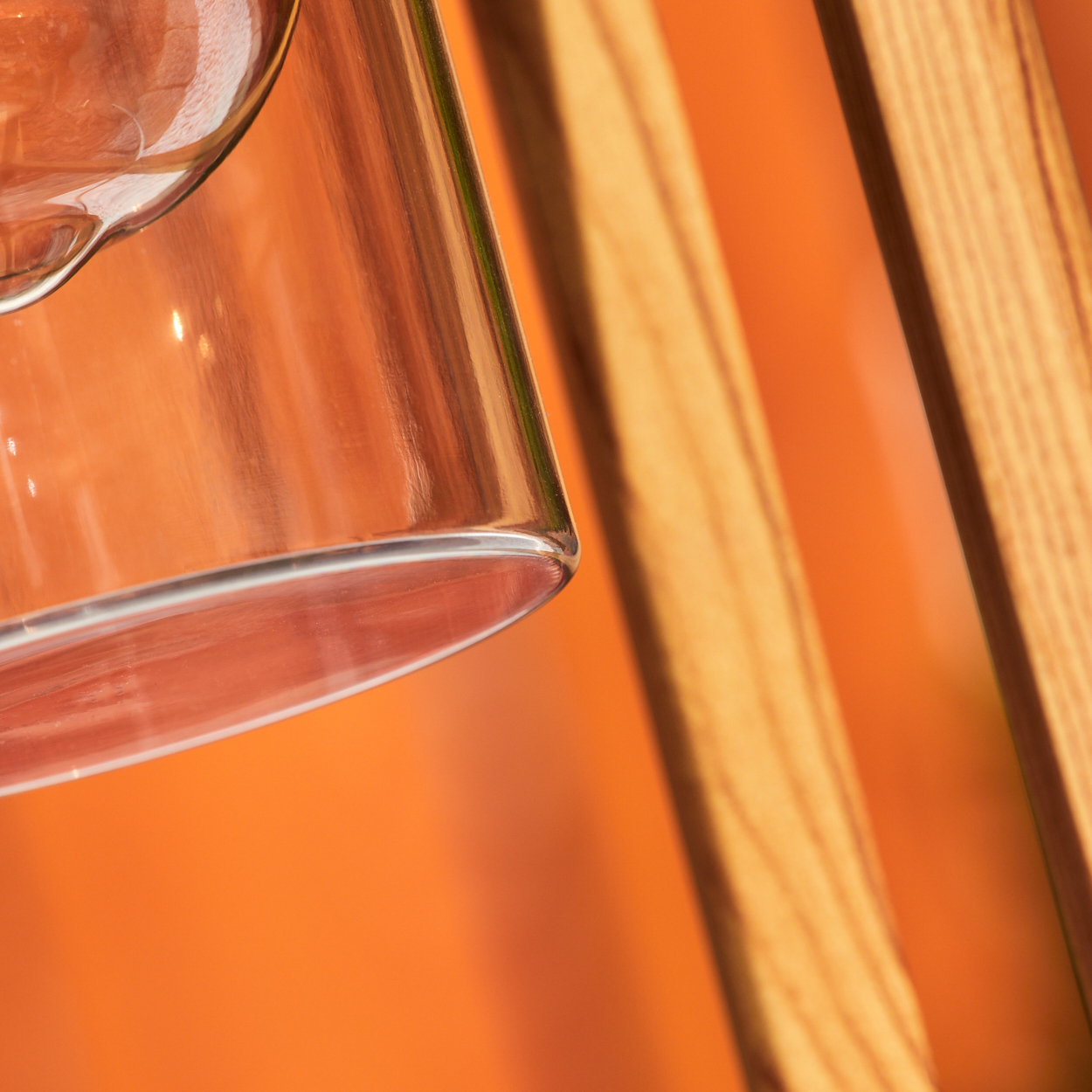 Nahaufnahme des Glaszylinders der Außenlampe, mit Holzrahmen und orangefarbenem Hintergrund.