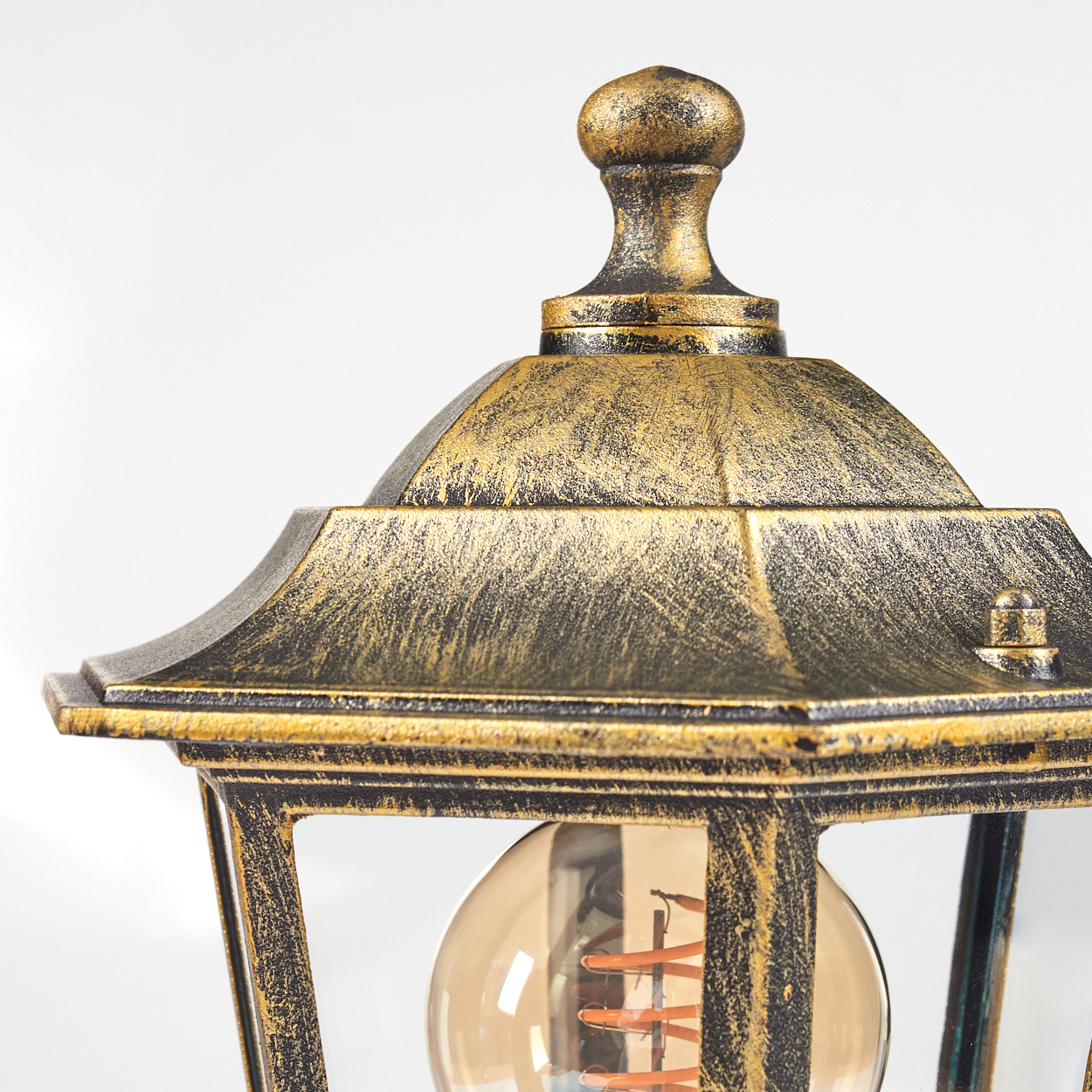 Nahaufnahme der Oberseite der goldenen Außenlampe. Aufwendige Details, Glühbirne darunter sichtbar.