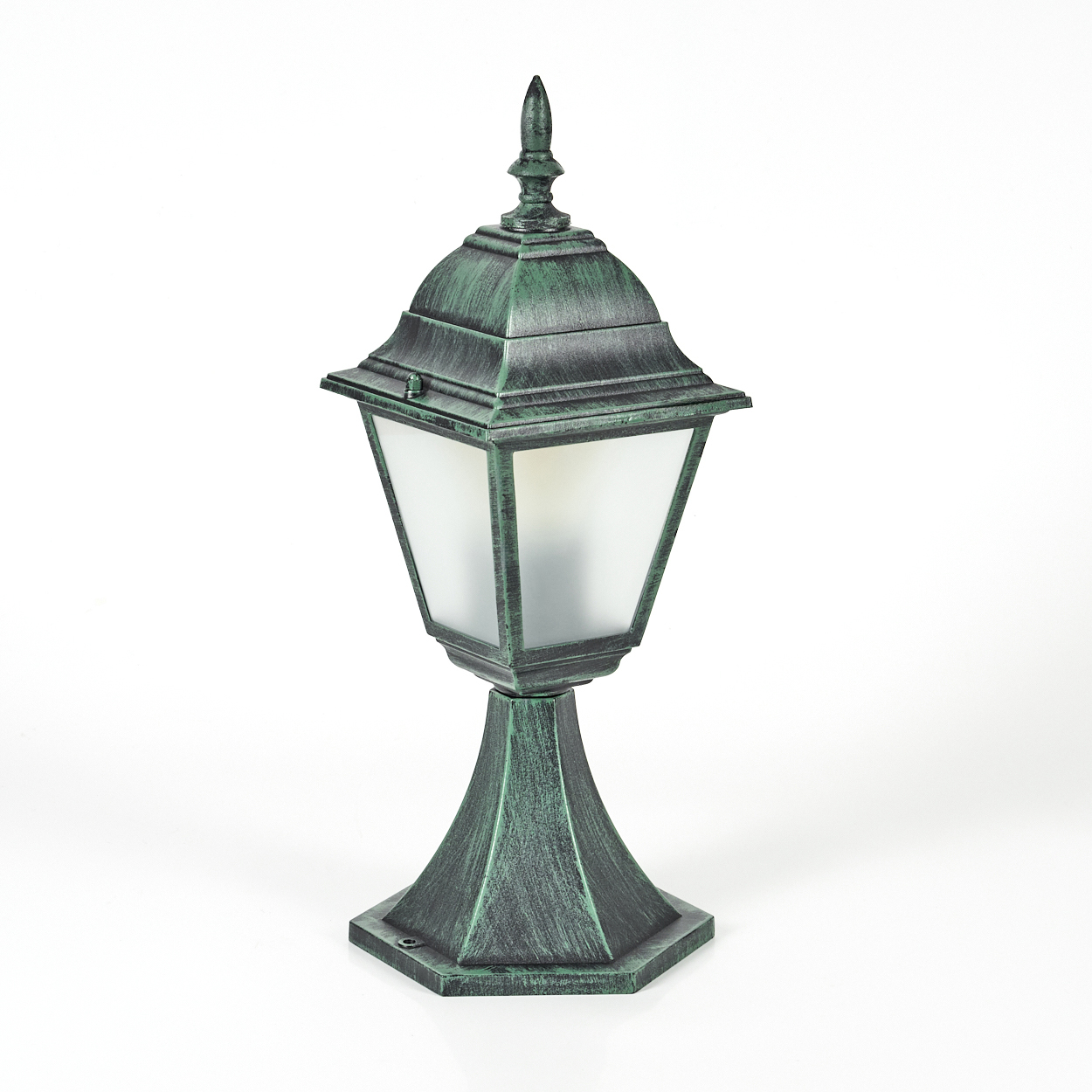 Eine grüne Außenlampe mit dekorativer Spitze und Sockel. Sie hat ein Milchglasgehäuse und steht auf weißem Untergrund.