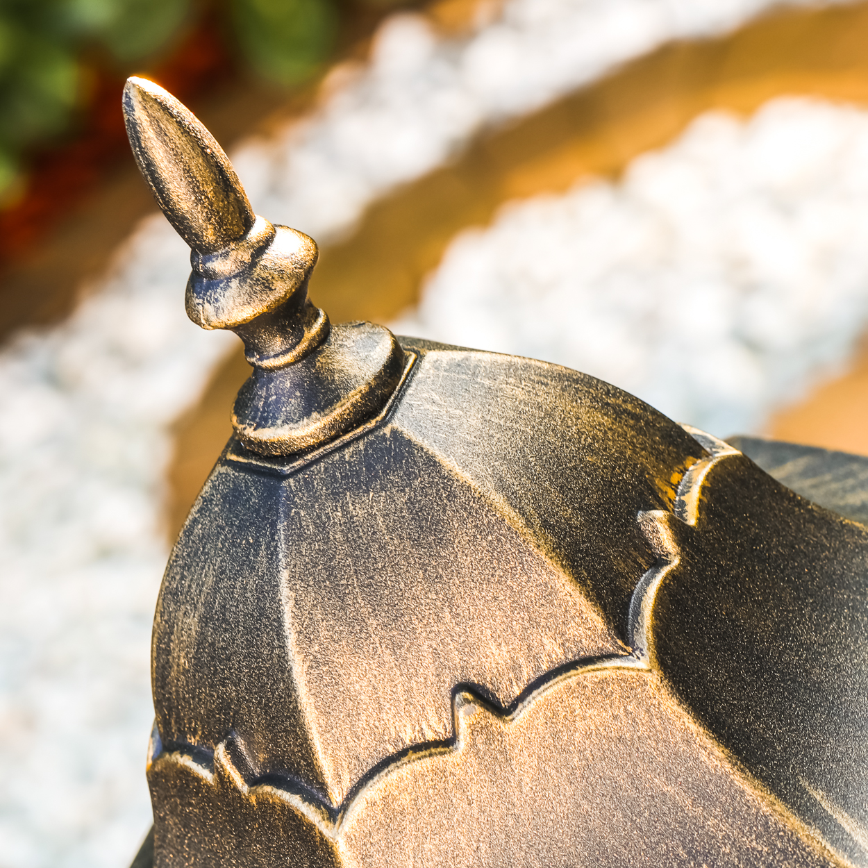 Nahaufnahme der Oberseite einer dekorativen Außenlampe. Die Lampe hat eine gold-schwarze Oberfläche und steht vor verschwommenem Hintergrund.