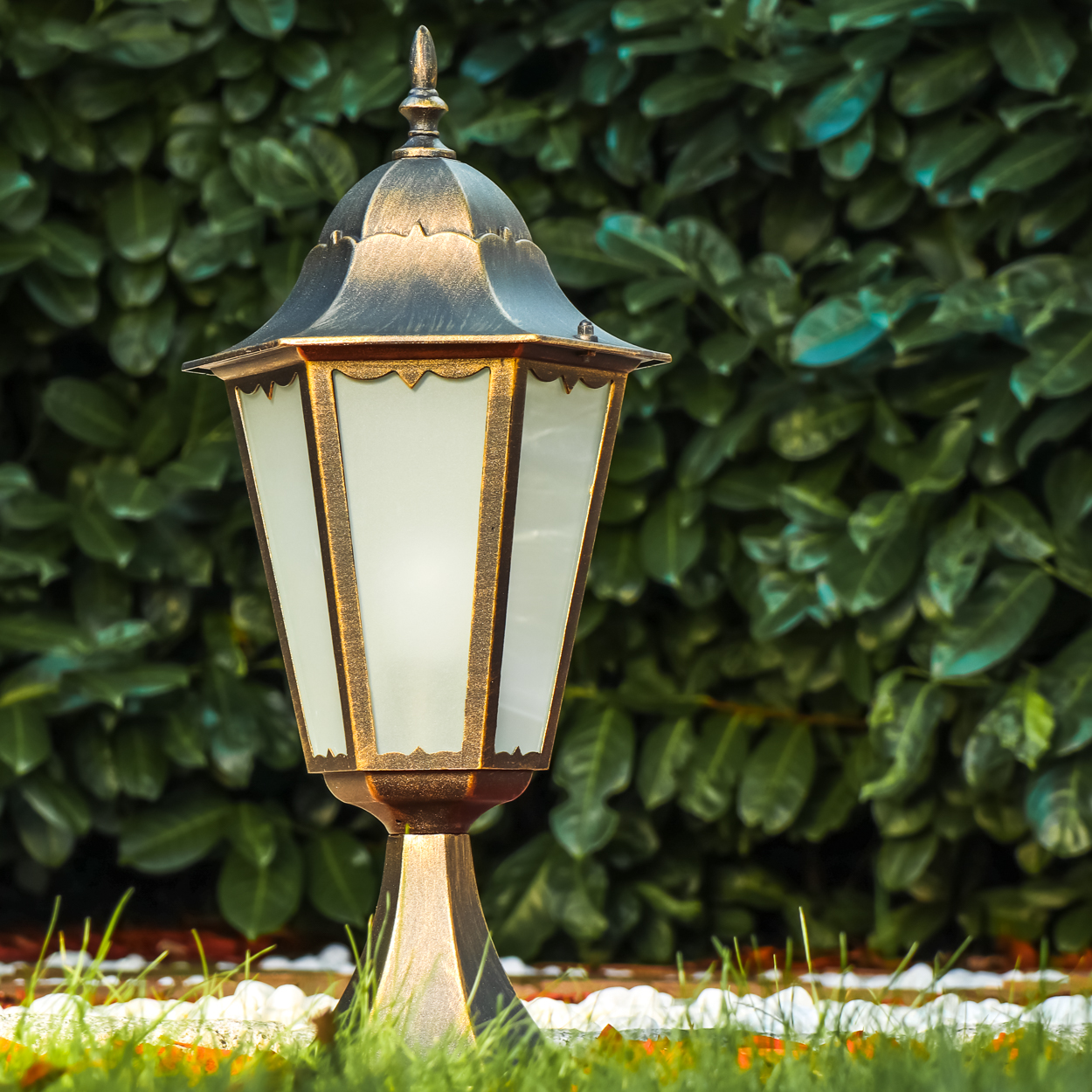 Eine dekorative Außenlampe im Garten. Die Lampe hat eine gold-schwarze Oberfläche und Milchglas.