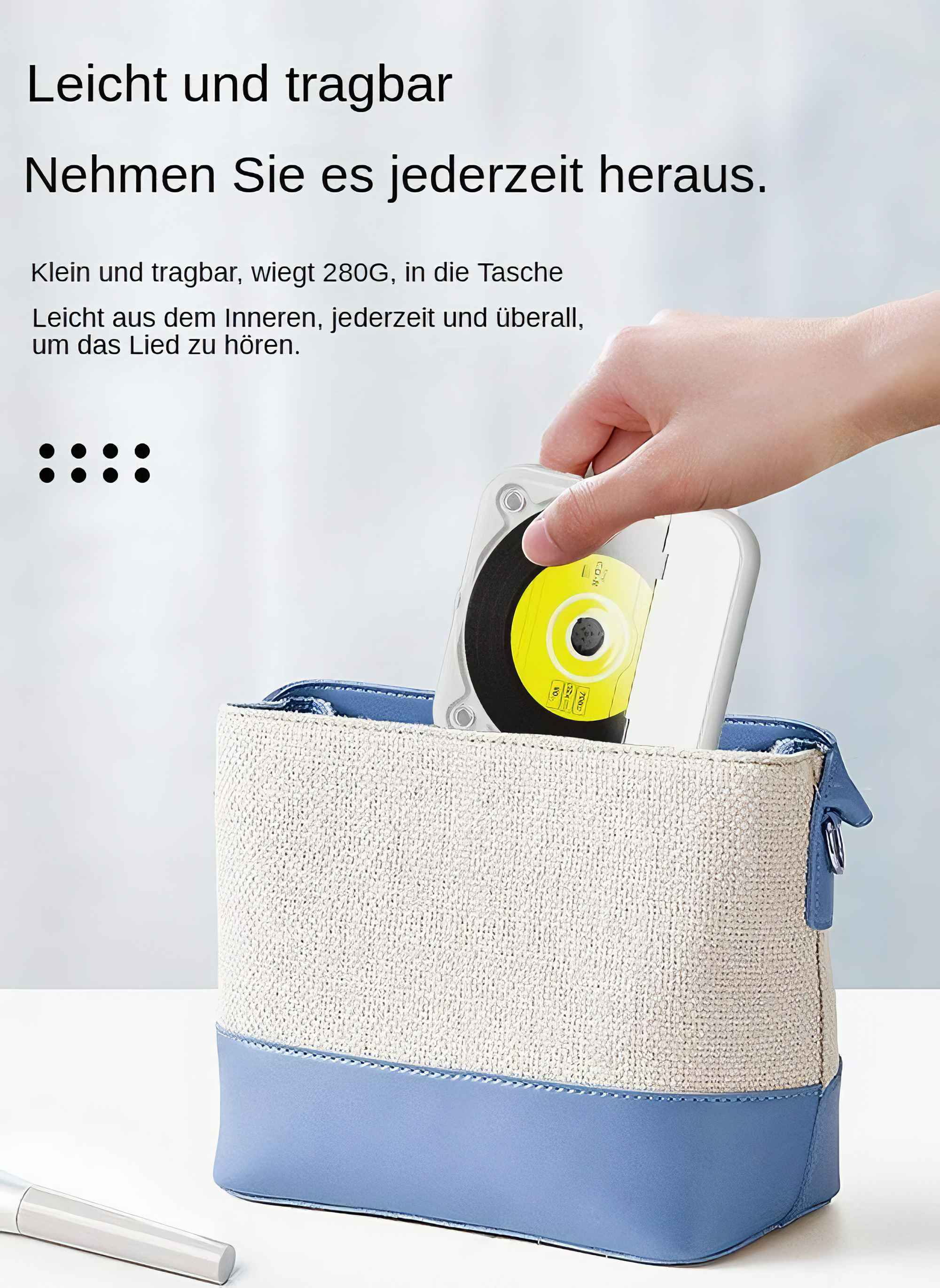 Eine Hand hält einen tragbaren CD-Player neben einer Handtasche auf blau-beige Hintergrund.