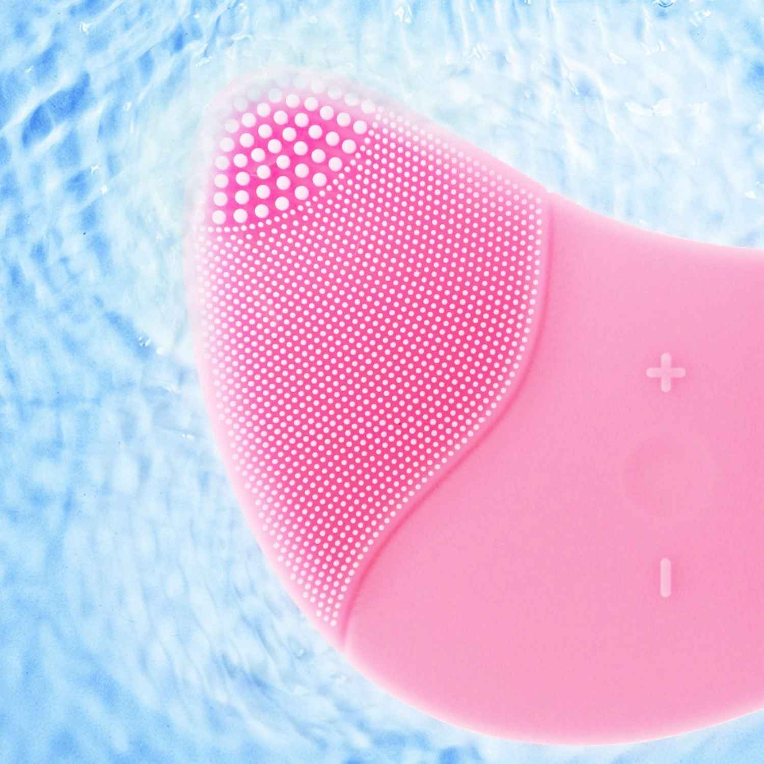 Nahaufnahme einer rosa Gesichtsbürste mit weißen Punkten auf der Bürstenoberfläche und blauem Wasserhintergrund.