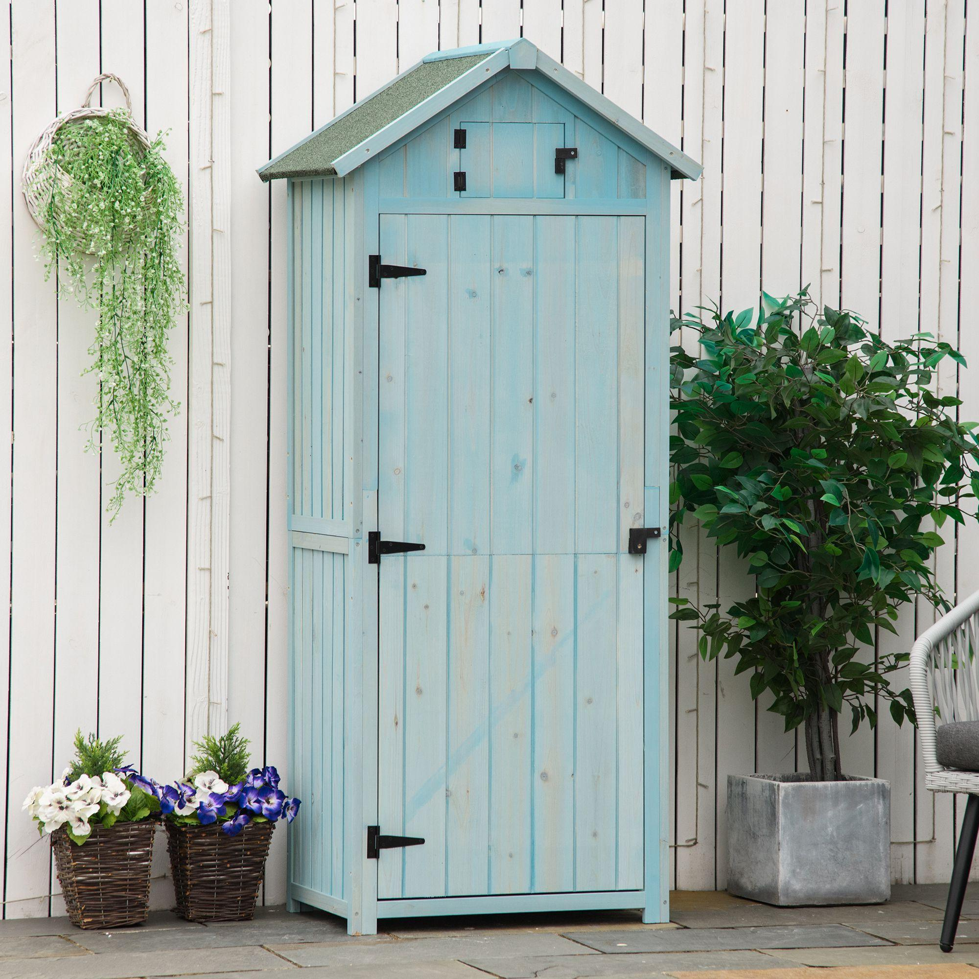 Ein blaues Gartenhaus aus Holz mit grünem Dach vor einem weißen Zaun.