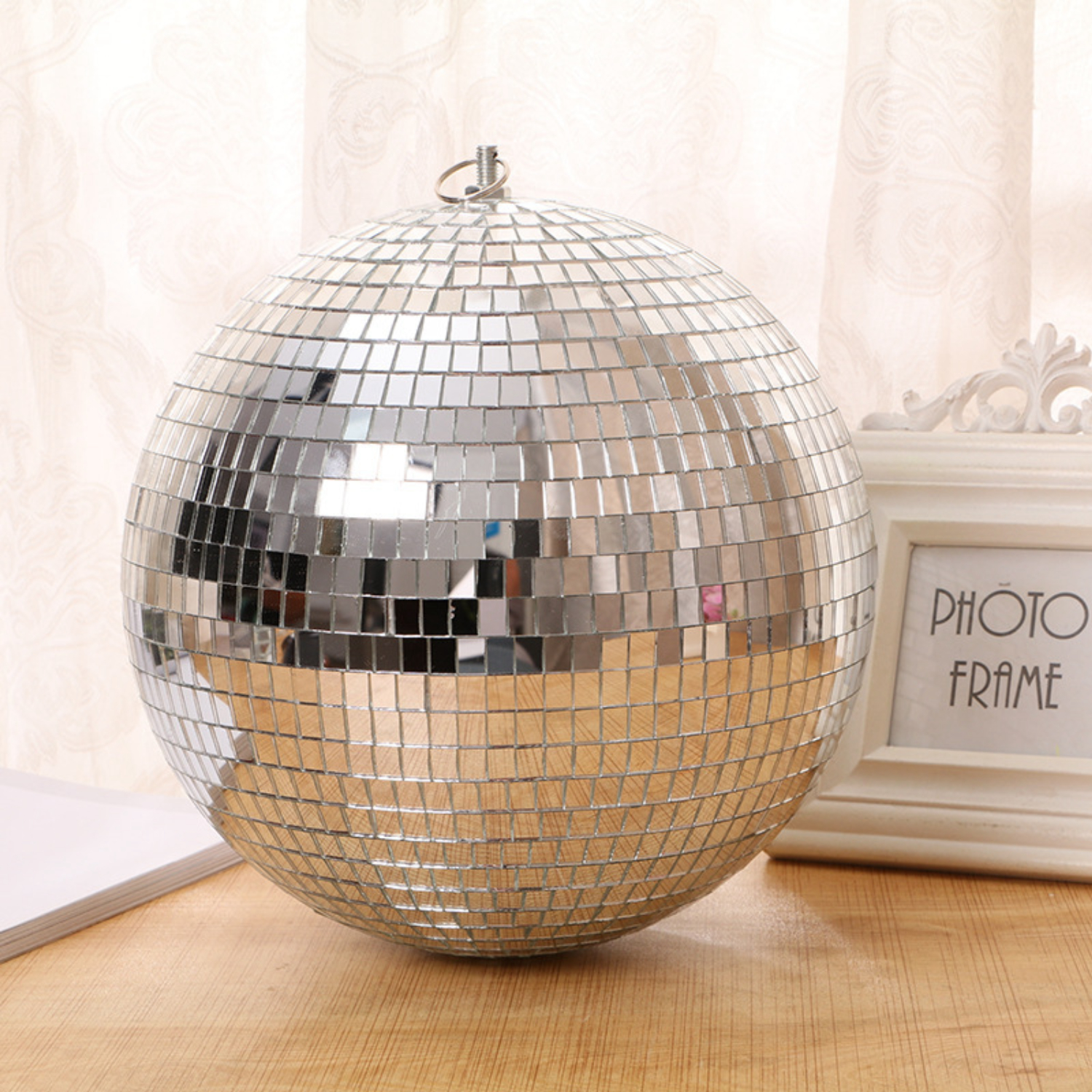 Eine silberne Discokugel auf einem Holztisch, mit einem Fotorahmen im Hintergrund.