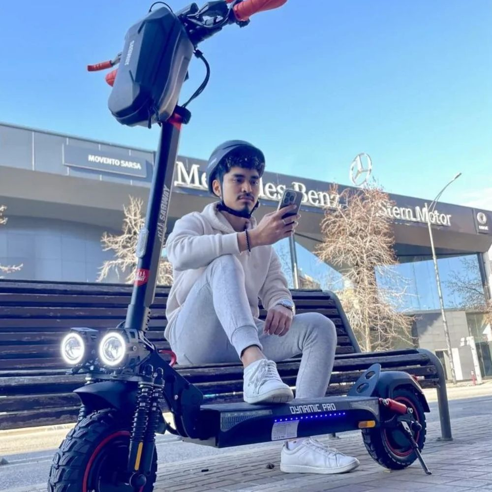 Un hombre sentado en un banco con un patinete eléctrico. Sostiene un teléfono.