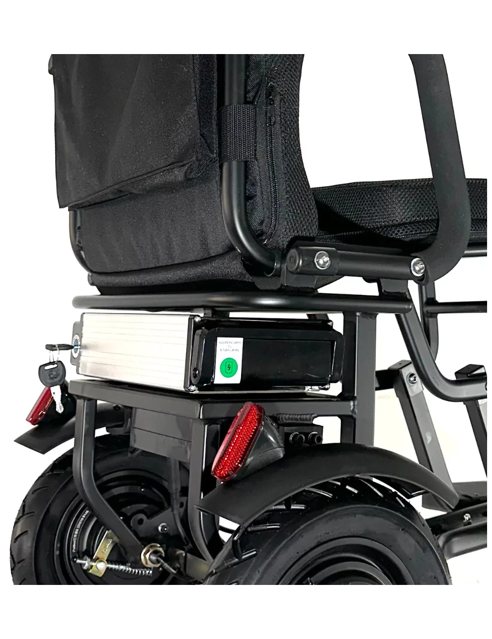 Un primer plano destaca el paquete de baterías y el conjunto de la rueda trasera de un scooter de movilidad negro sobre un fondo blanco.