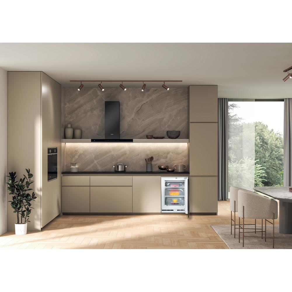 Cocina moderna con mini-nevera abierta mostrando alimentos. Armarios beige, salpicadero de mármol y una planta visibles.