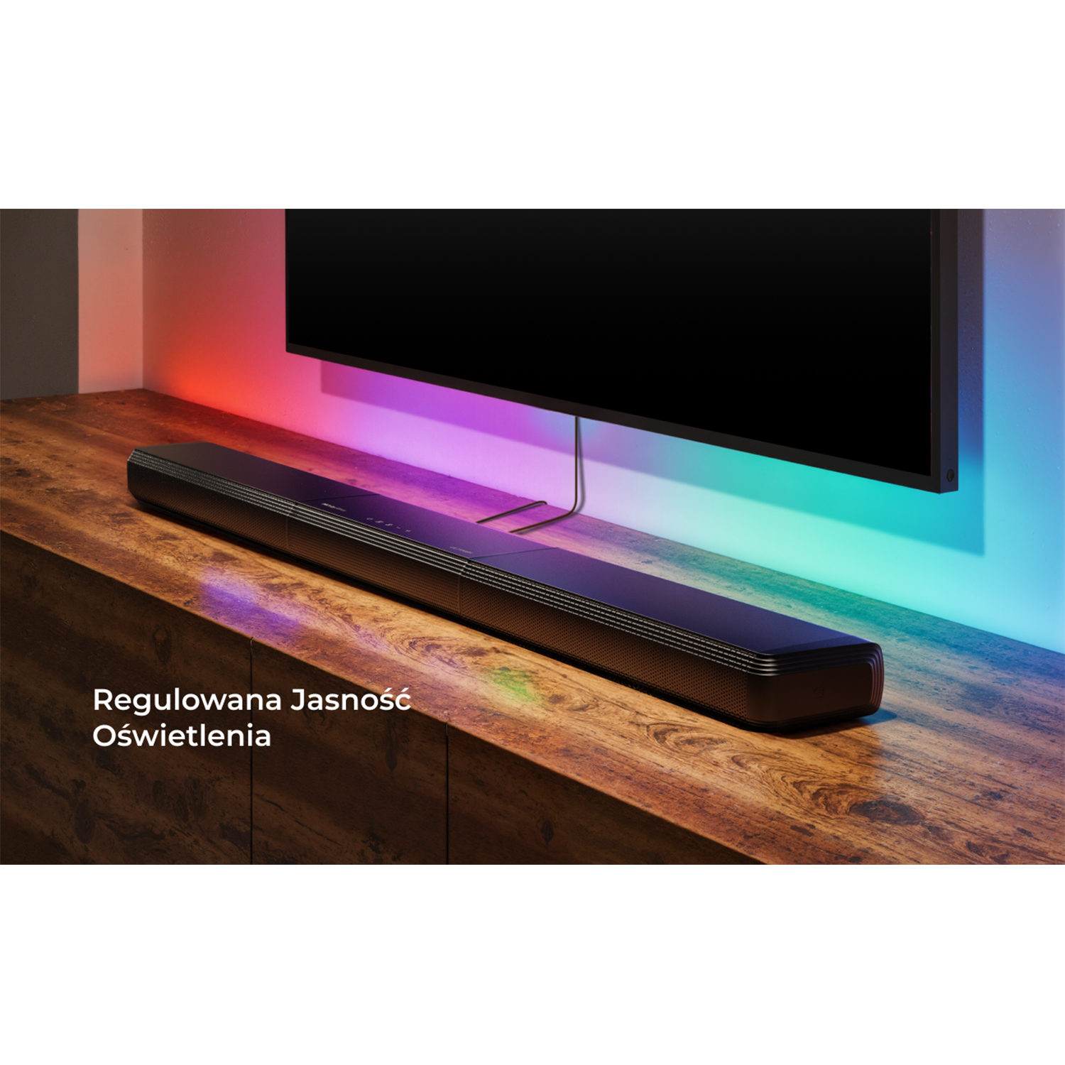 Telewizor na drewnianym stole. Soundbar znajduje się pod telewizorem. Tekst: Regulowana jasność.