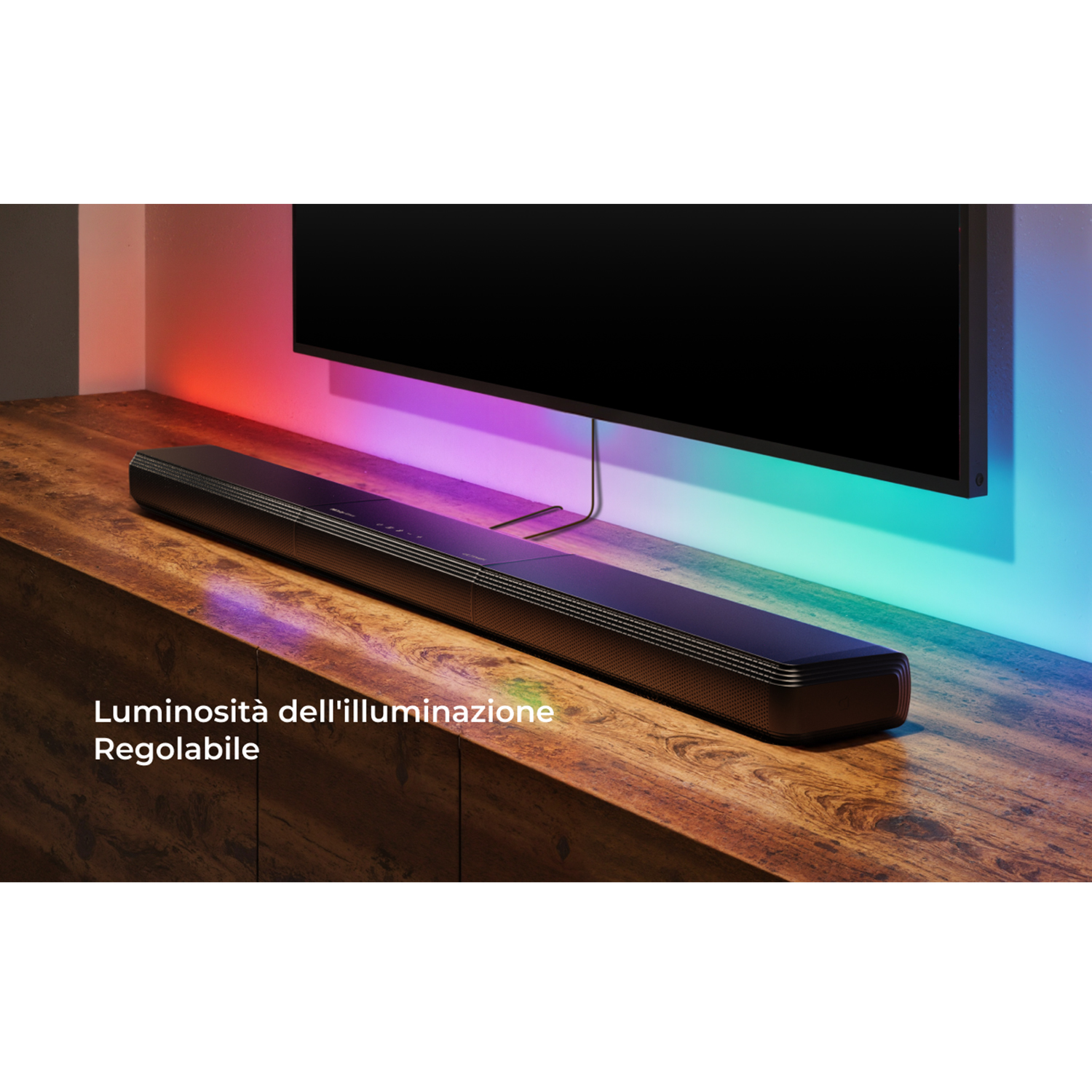 Una soundbar su una superficie di legno. Una TV a muro con retroilluminazione colorata.
