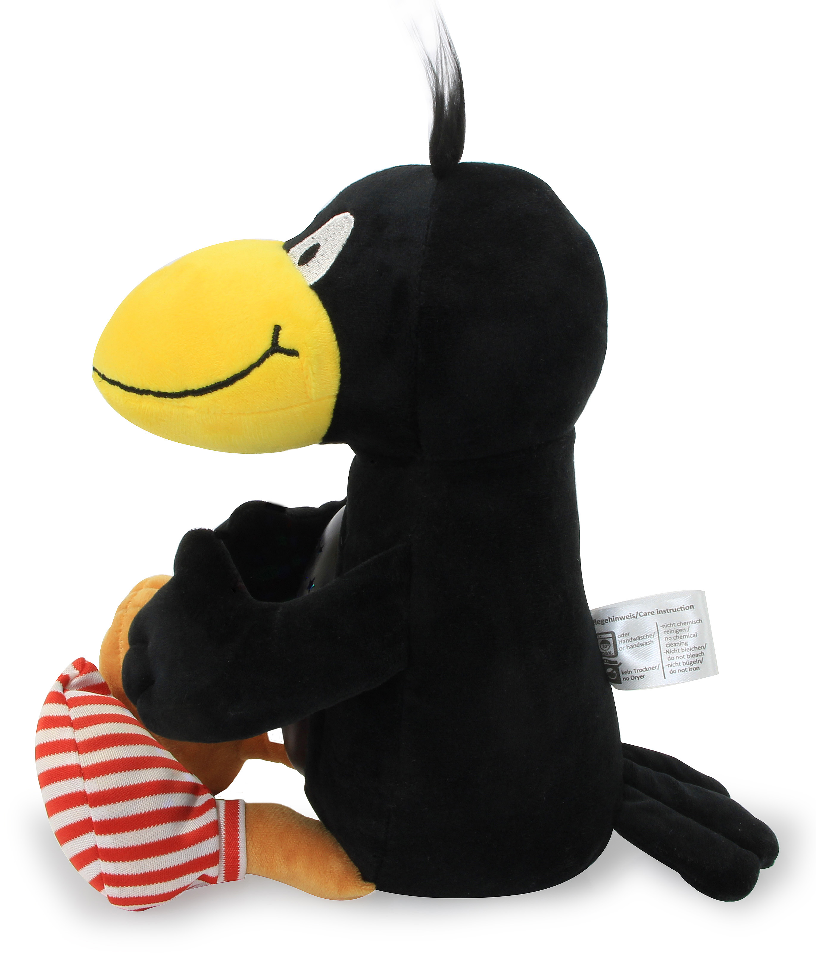 Schwarzes Stoffvogelspielzeug mit gelbem Schnabel. Es hält ein orangefarbenes Objekt und trägt rot-weiß gestreifte Socken.