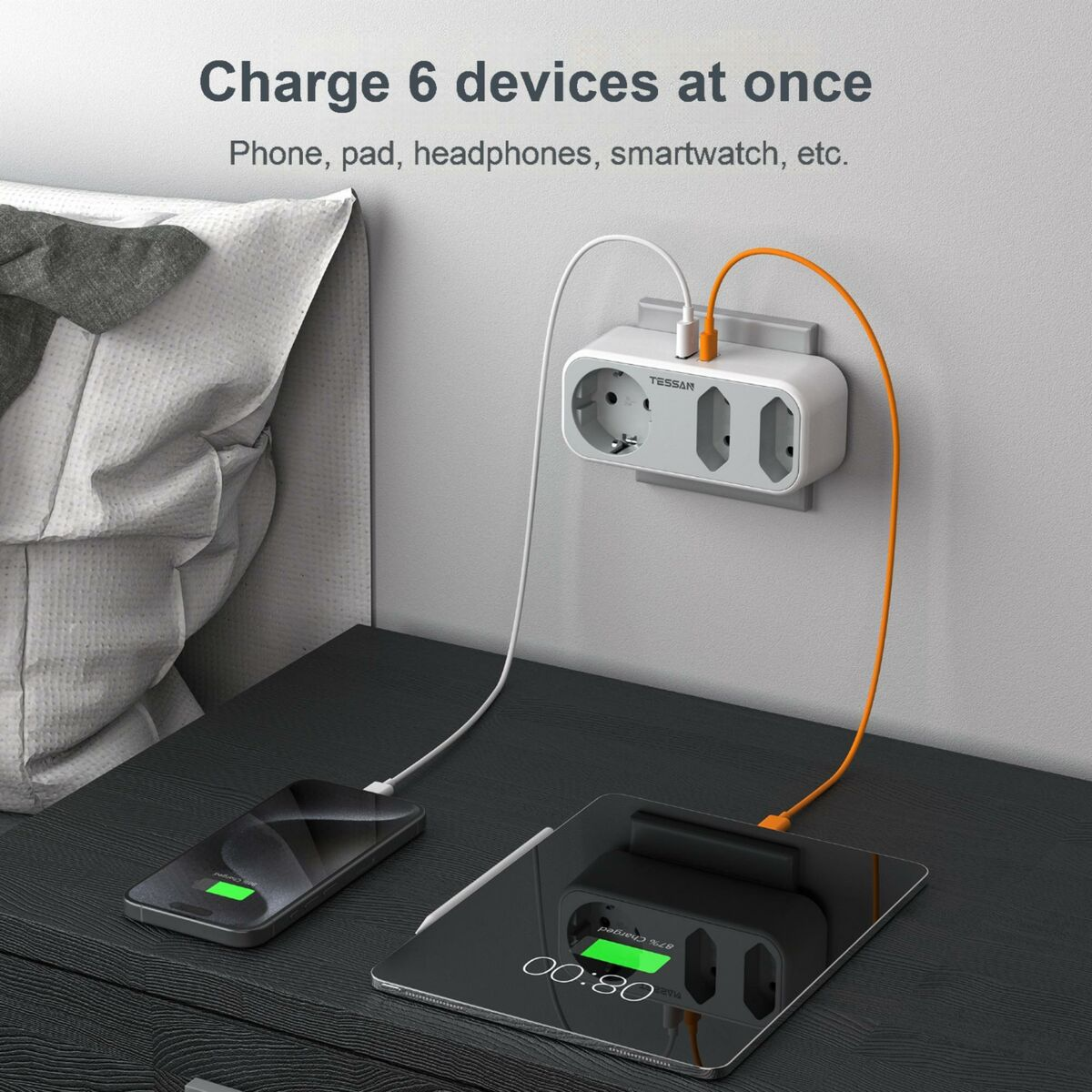 Un adaptador de corriente blanco en una mesita de noche cargando una tableta y un teléfono con TESSAN.