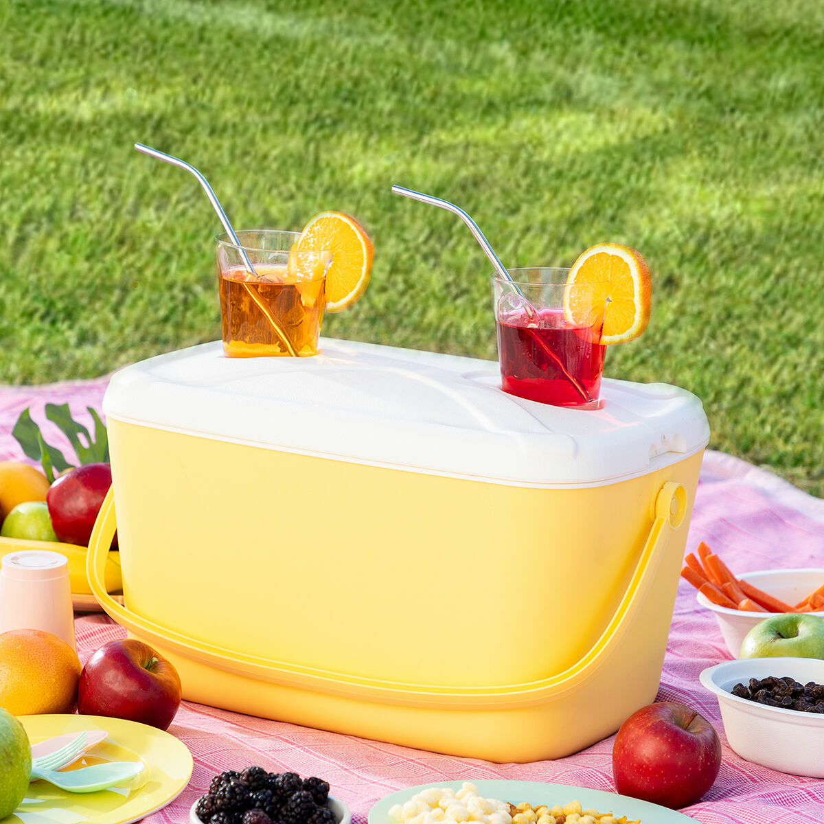 Una escena de picnic con una nevera amarilla, bebidas y comida en una manta.