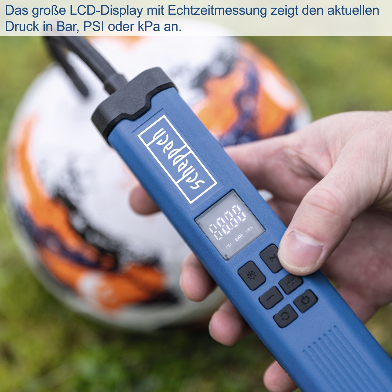 Eine Hand, die ein blaues digitales Reifenfüllgerät hält. Ein Fußball im Hintergrund.