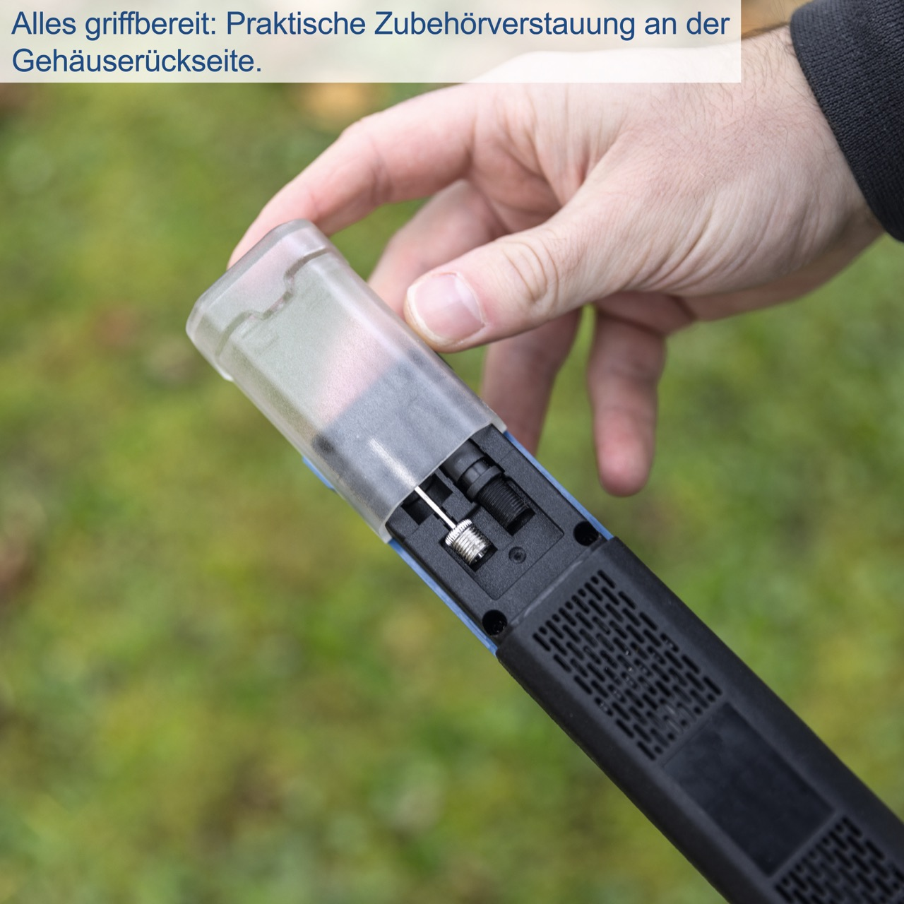 Eine Hand hält ein blaues Werkzeug mit einem Bildschirm und einer transparenten Kunststoffabdeckung, vor grünem Hintergrund.