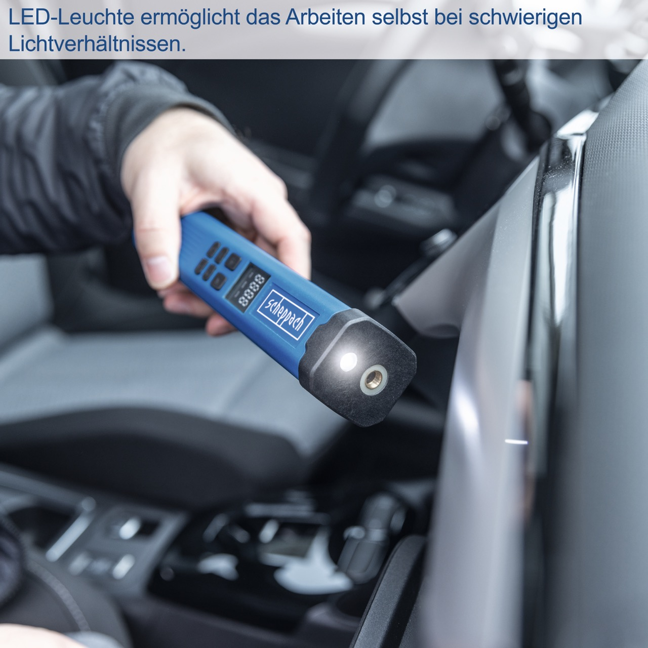 Hand hält ein blaues Werkzeug mit Licht an, in einem Auto. Das Licht scheint auf das Auto.