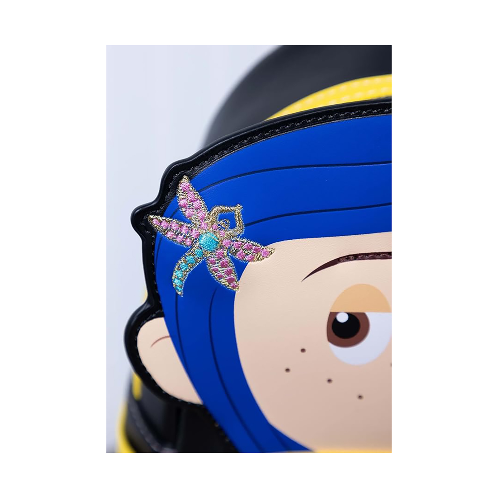 Primo piano di uno zaino di Coraline con una forcina a forma di libellula sui capelli blu.