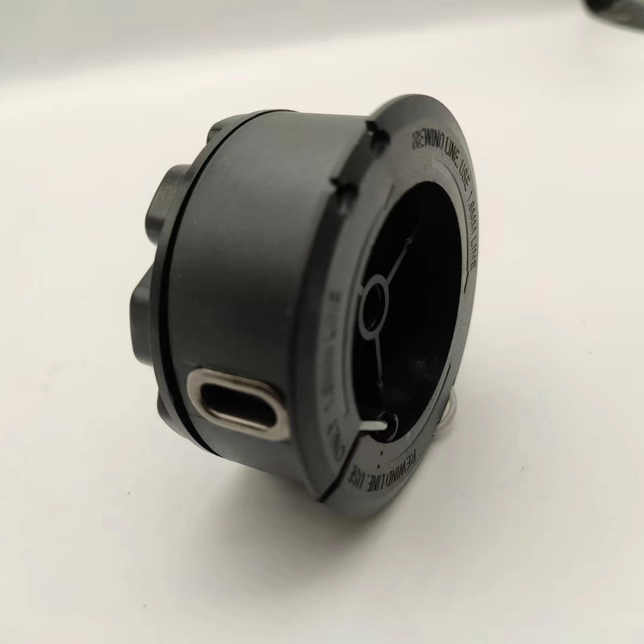 Eine schwarze Trimmerkopfkomponente mit einer Metallöse vor einem weißen Hintergrund.