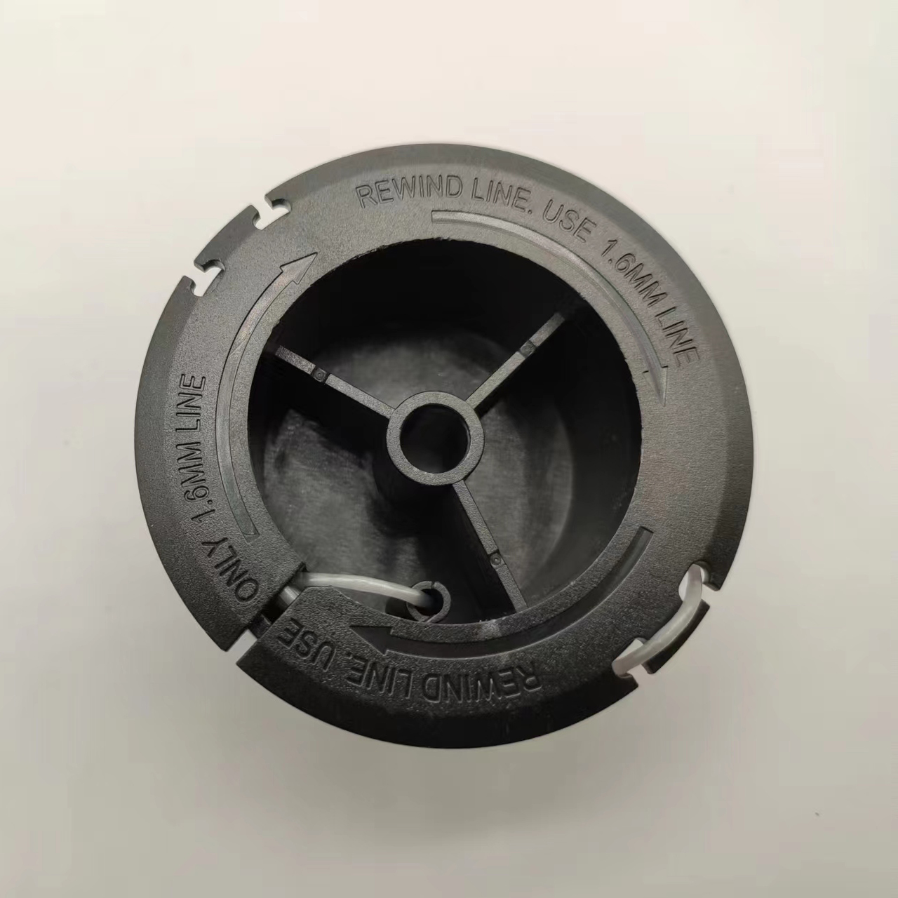 Schwarze Kunststoffspule mit Text. Der Text lautet: REWIND LINE. USE 1,6MM LINE. Die Spule befindet sich auf einer weißen Oberfläche.
