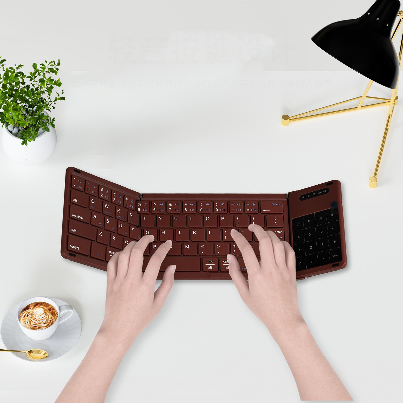 Hände benutzen eine braune, faltbare Tastatur auf weißer Oberfläche. Kaffeetasse und Pflanze sichtbar.