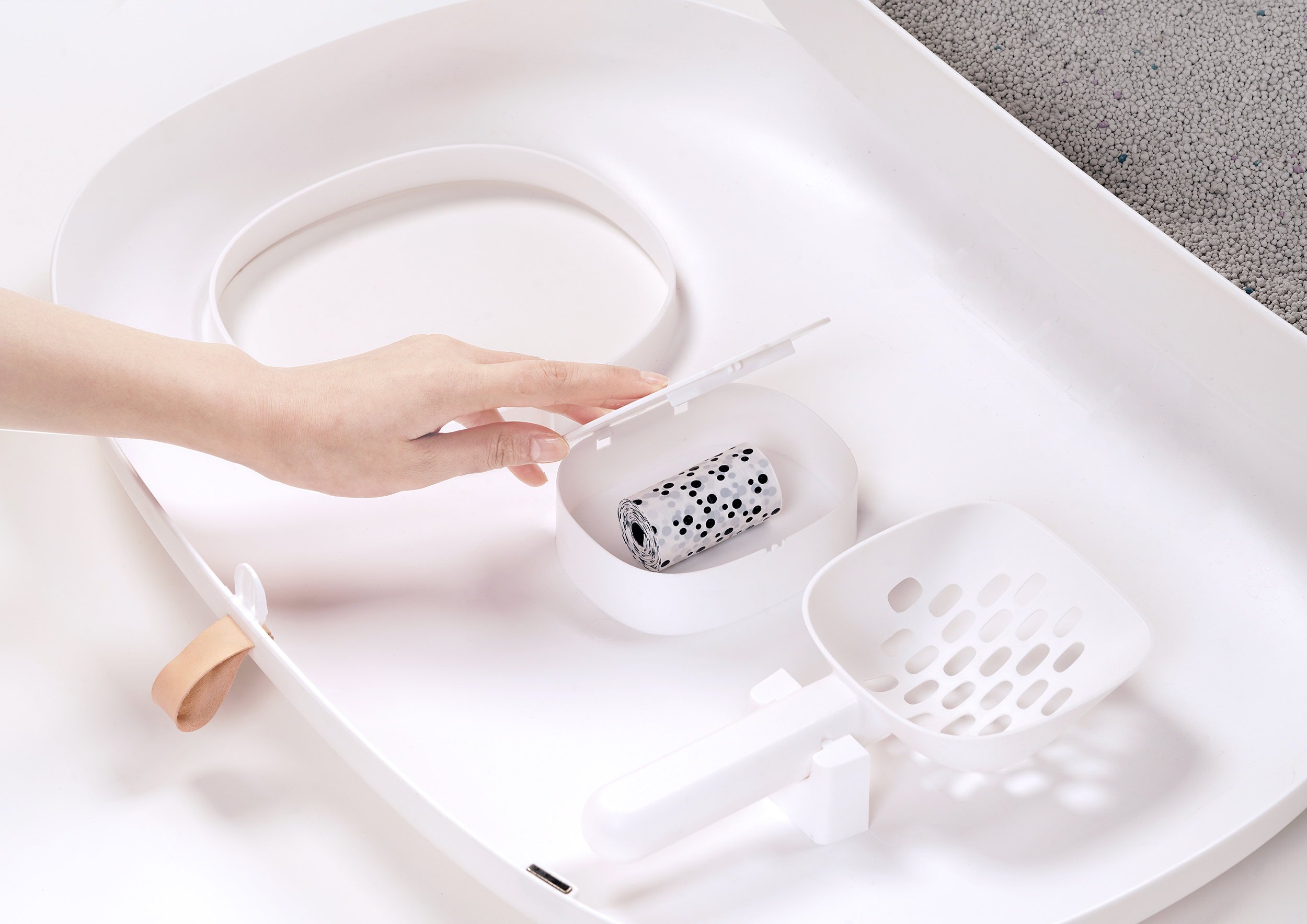 Eine Hand öffnet ein Fach einer Katzentoilette und zeigt eine Rolle Müllbeutel.