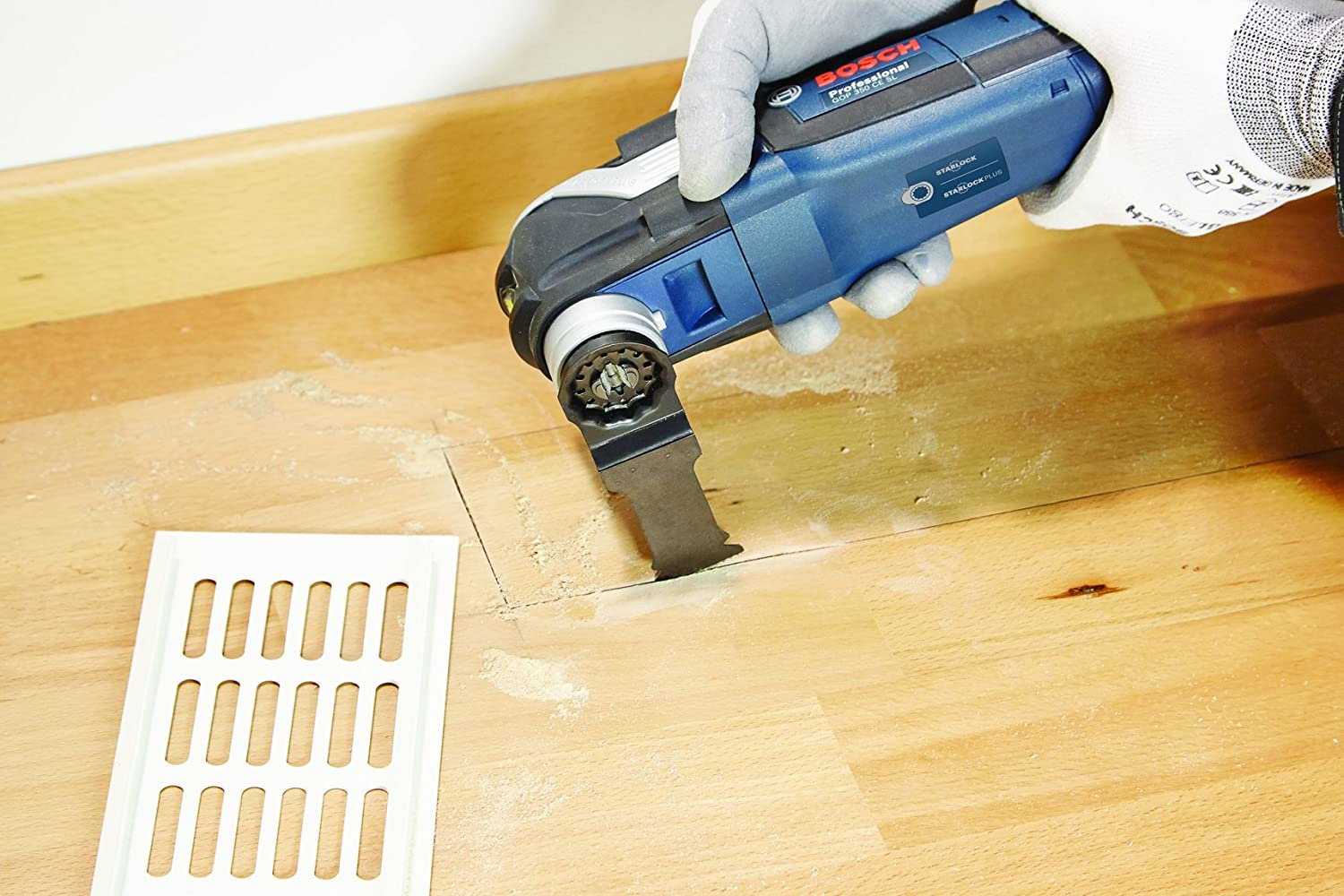 Eine Person verwendet ein Bosch Multi-Tool, um in eine Holzoberfläche zu schneiden. Das Werkzeug ist blau und schwarz.